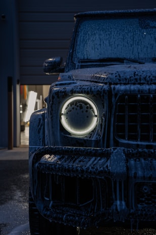 Dark suv covered in foam with glowing headlight.