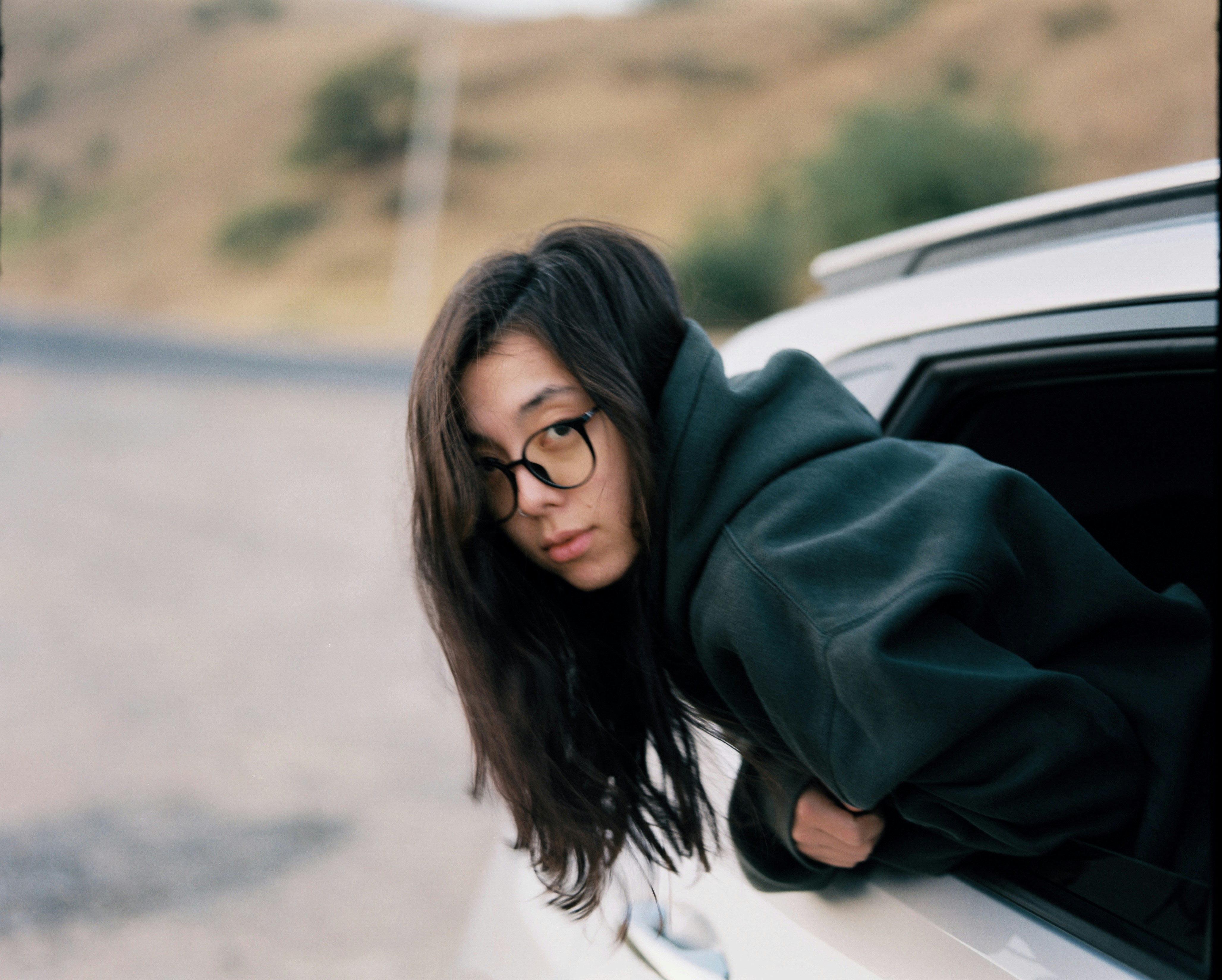 Young woman with glasses leans out car window