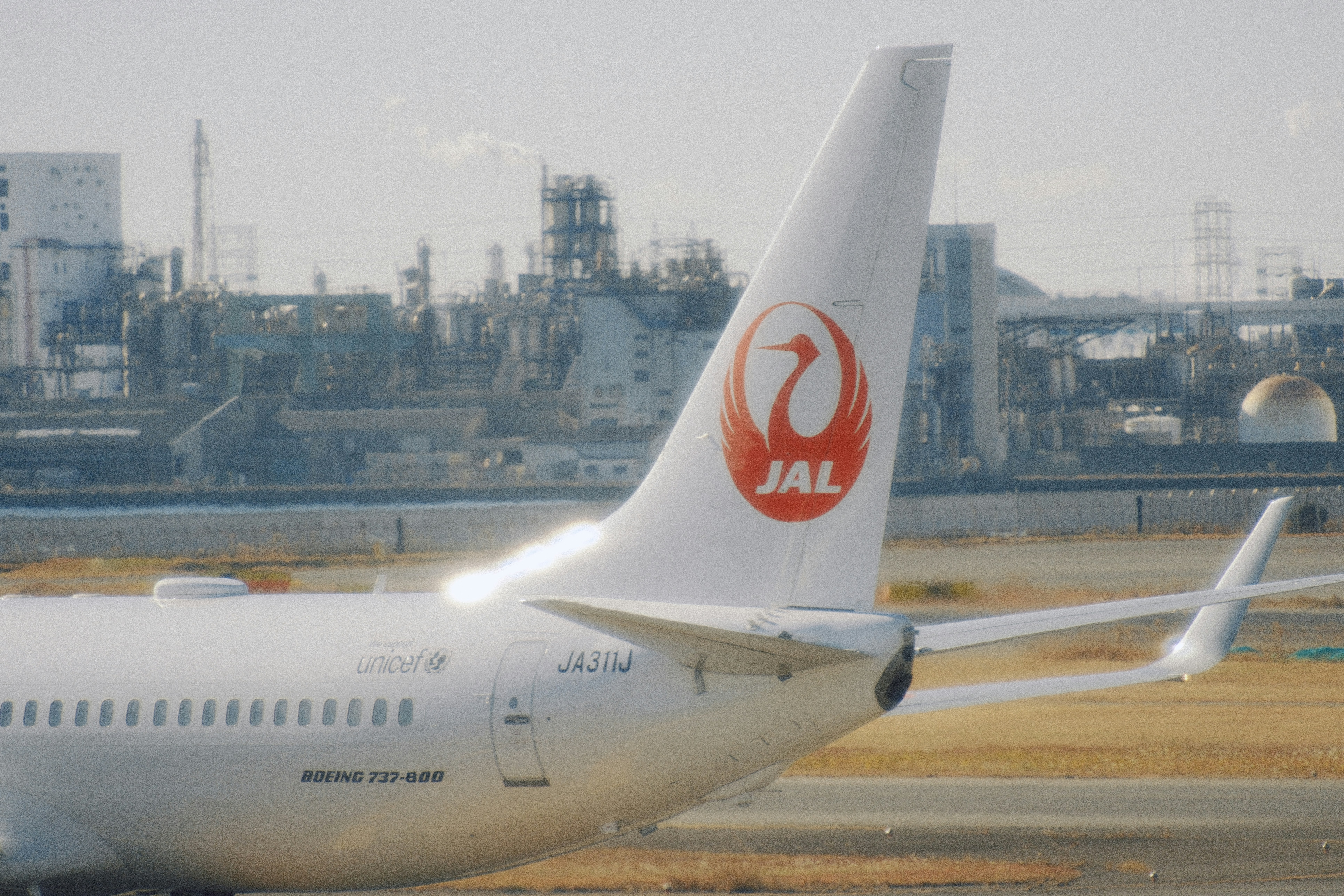 Japan airlines airplane tail with industrial background Via Unsplash (by Will Xiang)