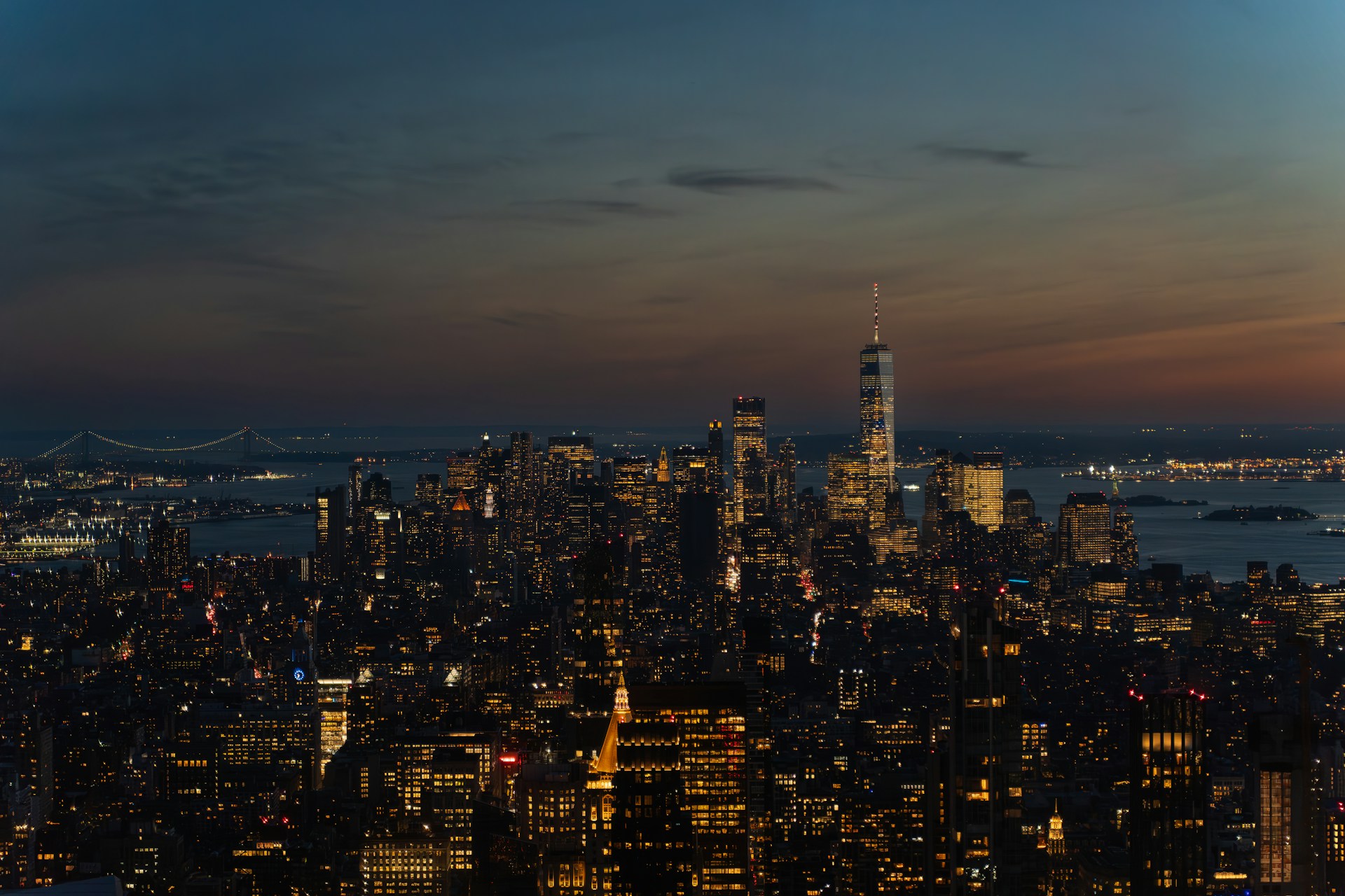 City skyline illuminated at dusk with distant bridge.