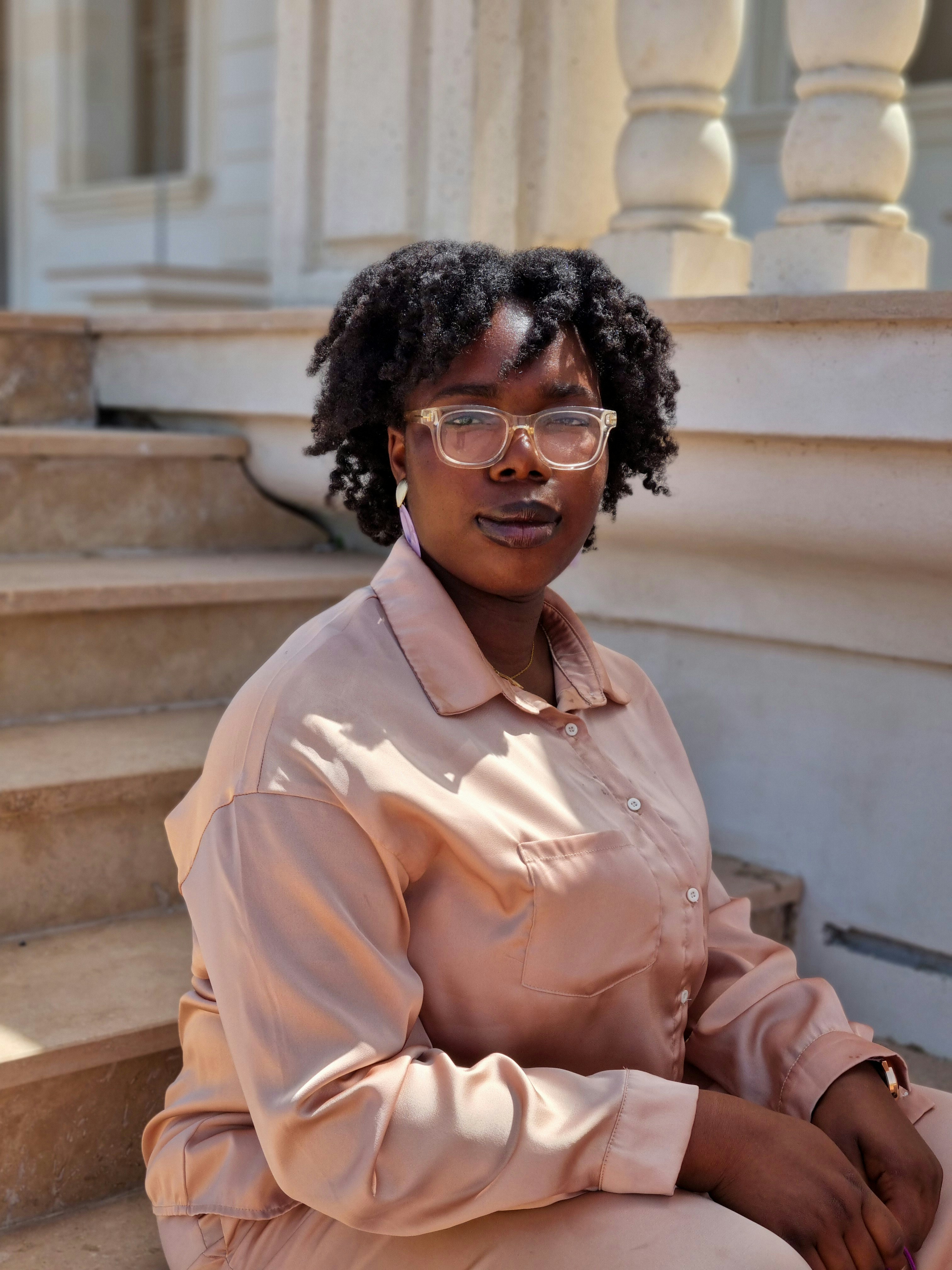 Young black woman with glasses sits on steps.