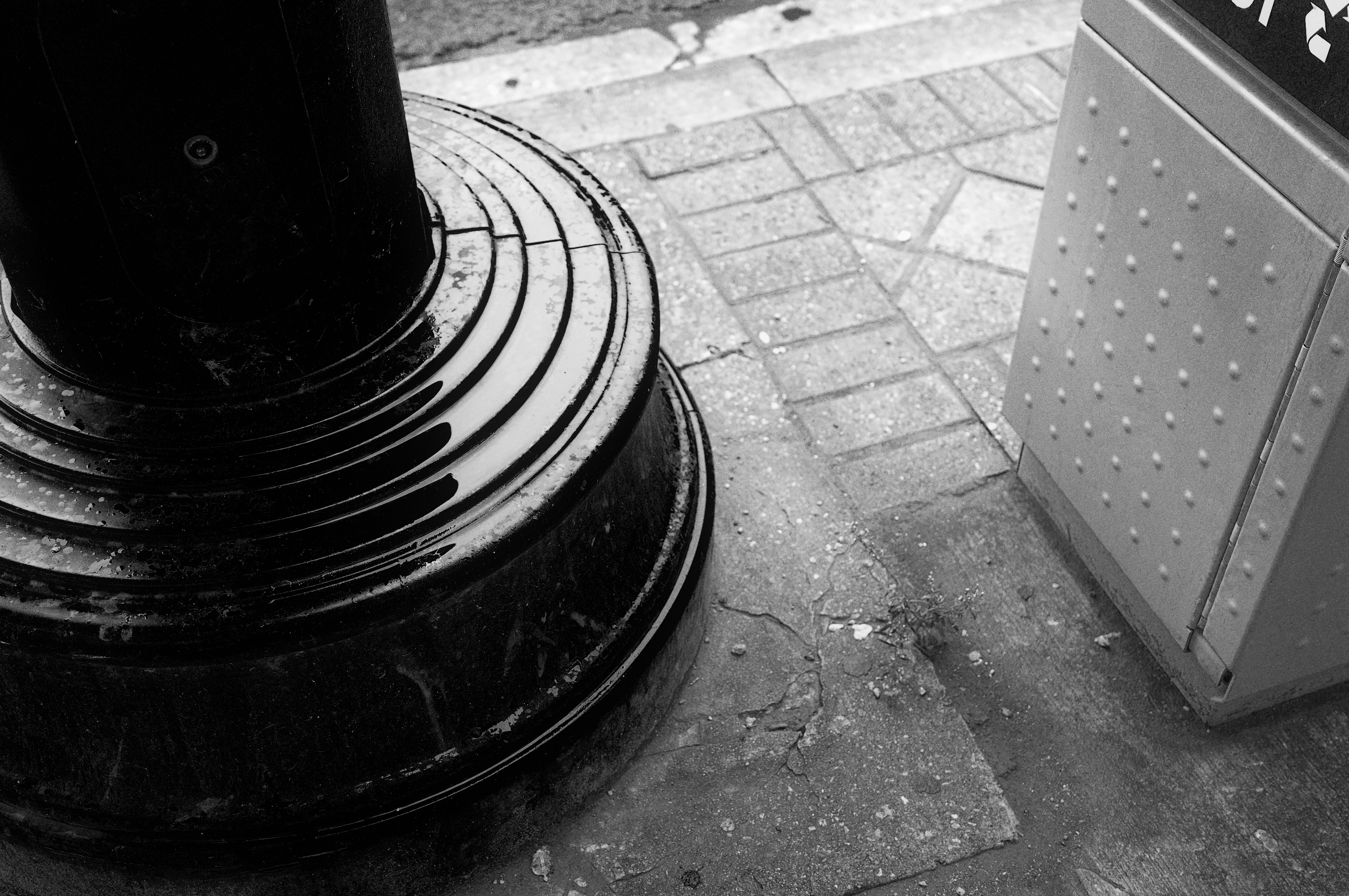 Black lamppost base on wet pavement with metal box.