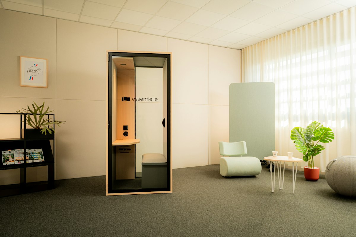 Cabine téléphonique acoustique vitrée dans un espace de travail clair, avec fauteuil, table basse et plantes