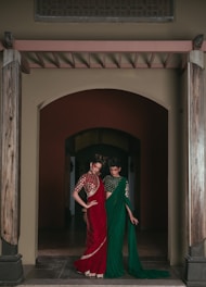 Two women in traditional indian saris stand under an archway.