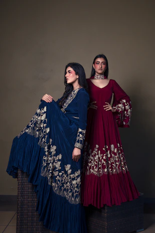 Two women in ornate gowns posing against a muted background.
