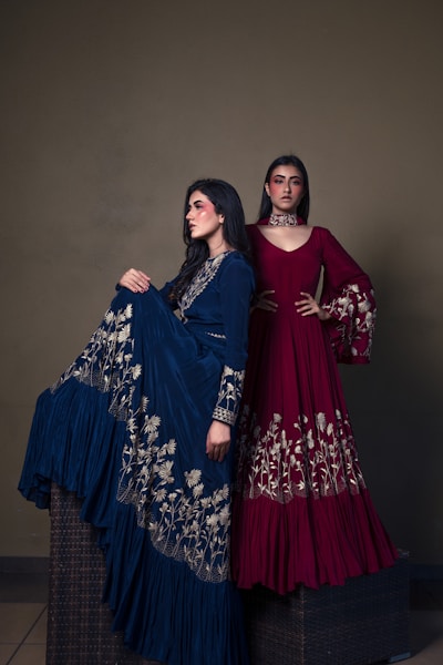 Two women in ornate gowns posing against a muted background.