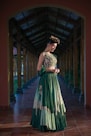 Woman in a green embroidered lehenga outfit poses elegantly.
