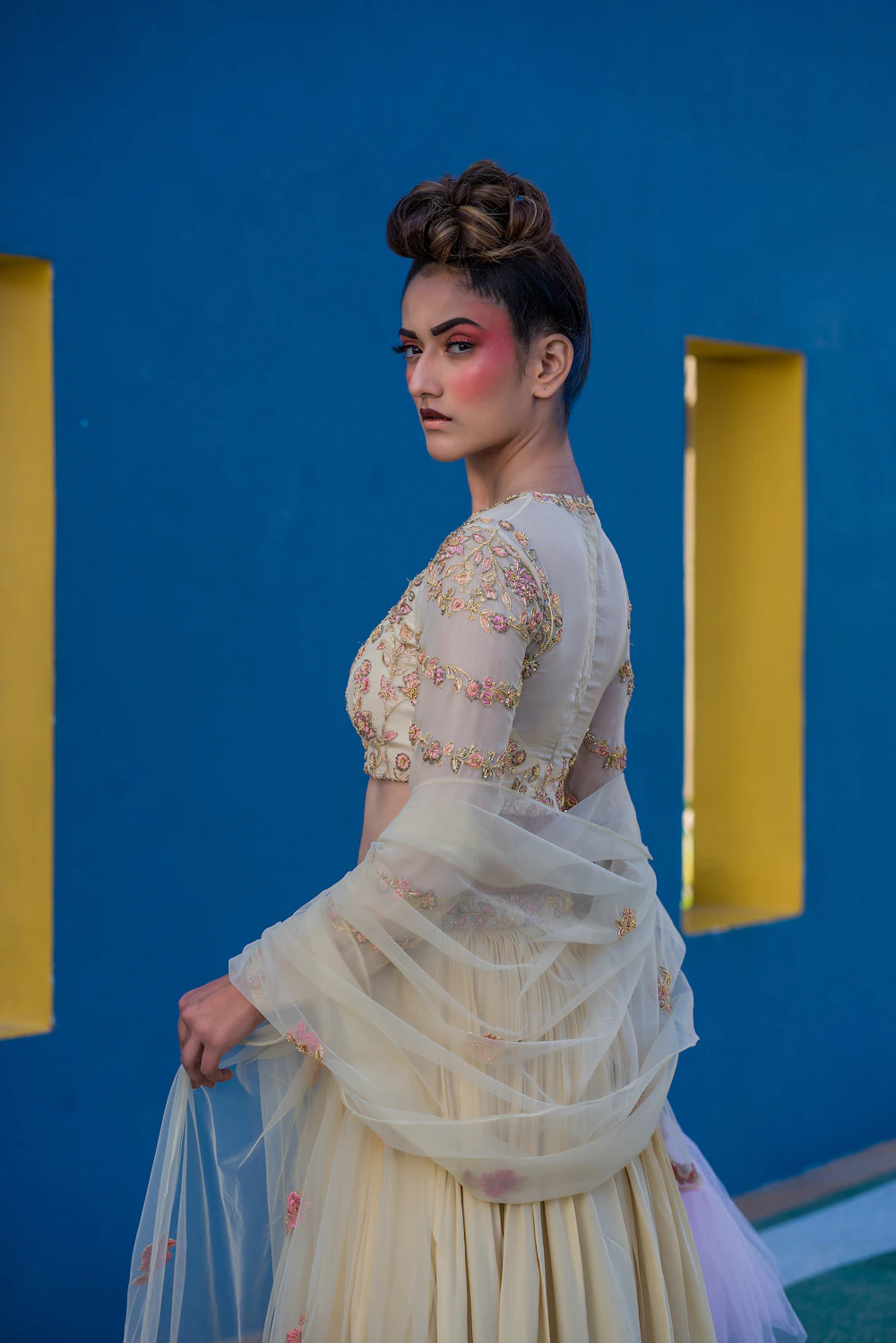 Model in an embroidered dress against a blue wall
