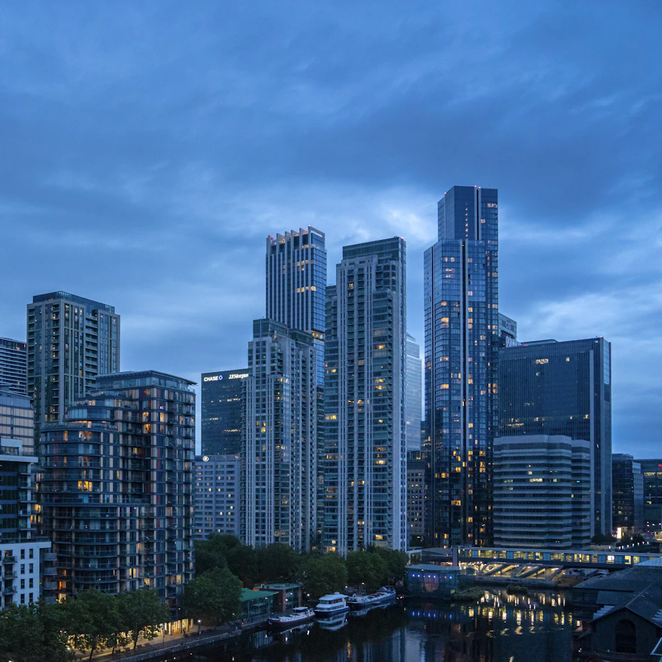 City skyline at dusk with tall buildings illuminated by warm lights against dark blue sky