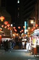People walk down a street lined with red lanterns at night.