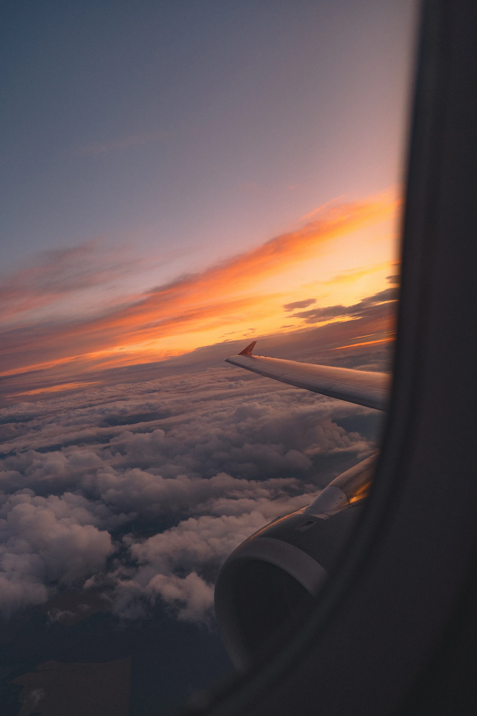 An airplane wing and engine above a layer of clouds with a warm golden sunset behind
