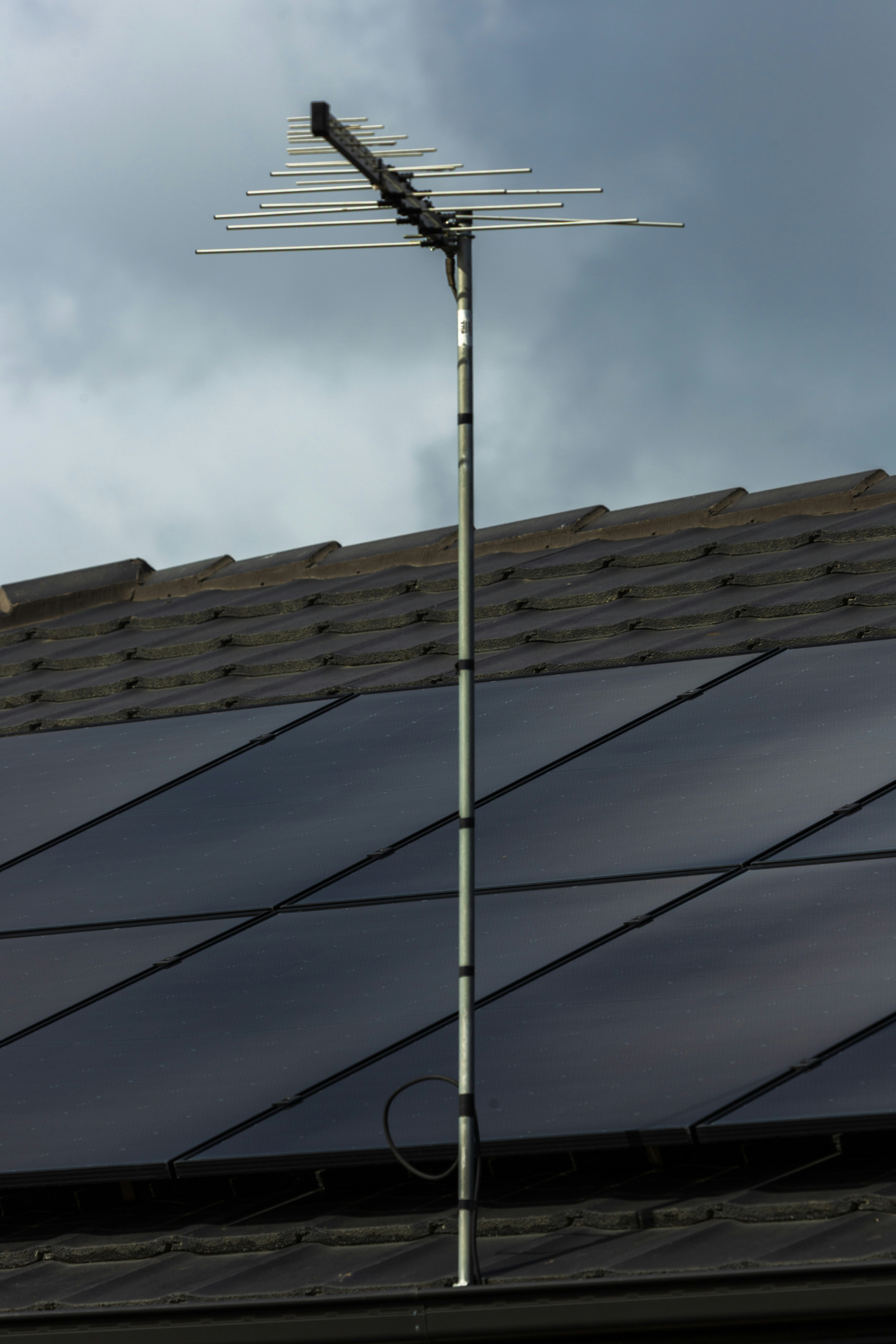 Rooftop solar panels with TV antenna under stormy clouds.