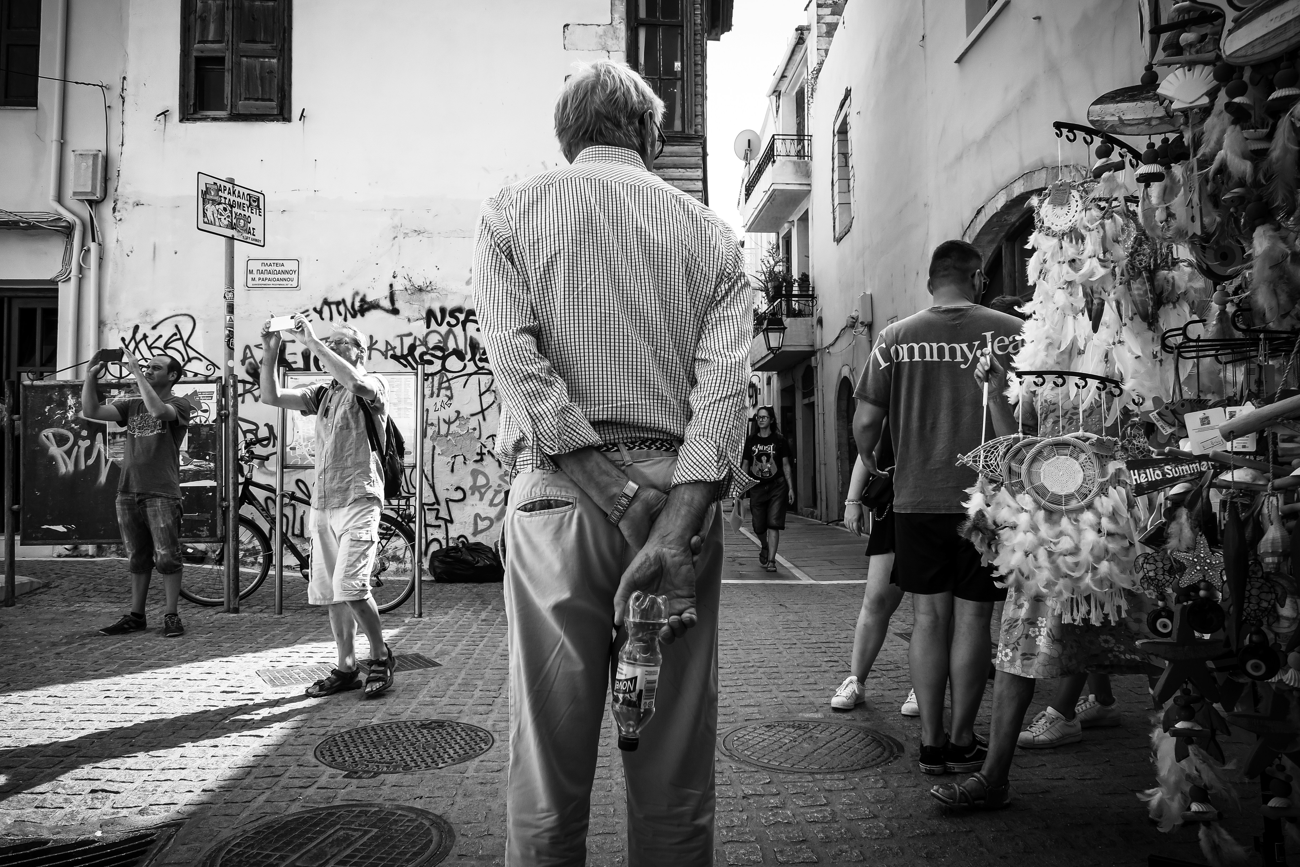 Elderly man stands with hands behind back on street.