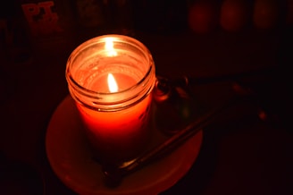A lit red candle in a glass jar.