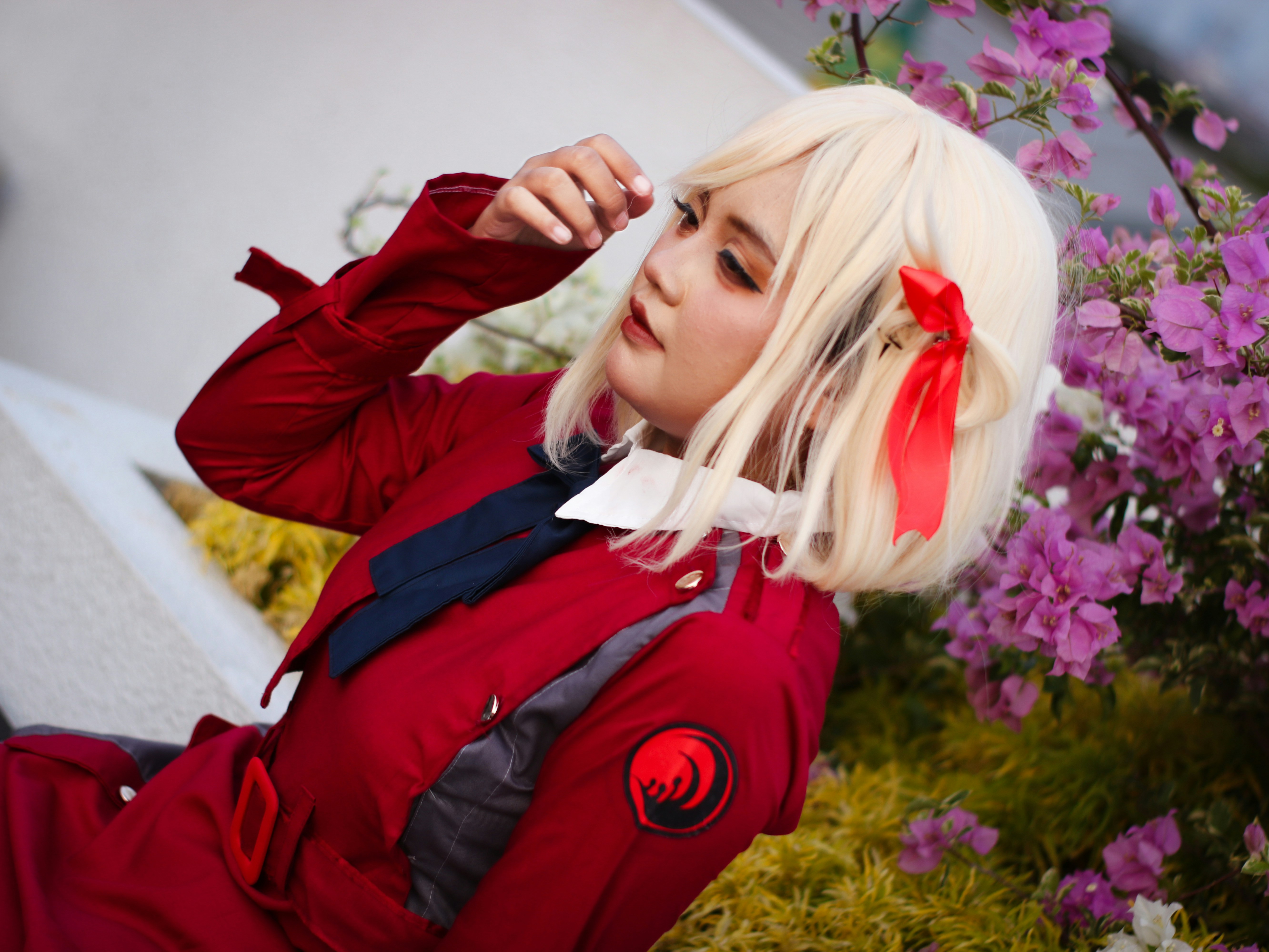 A vibrant outdoor cosplay portrait featuring a blonde-haired character with a red ribbon