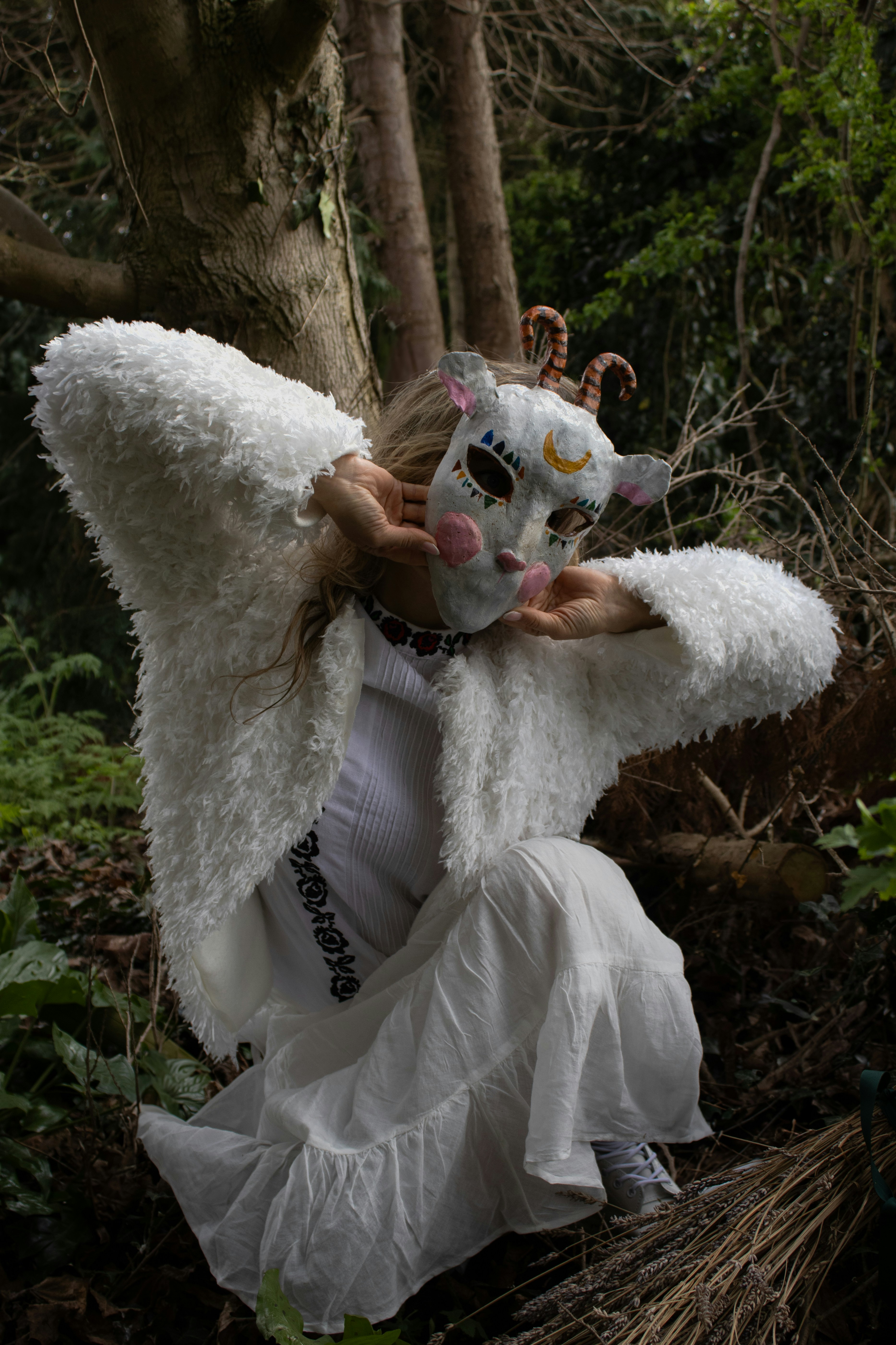 Woman in goat mask and white fur coat in forest