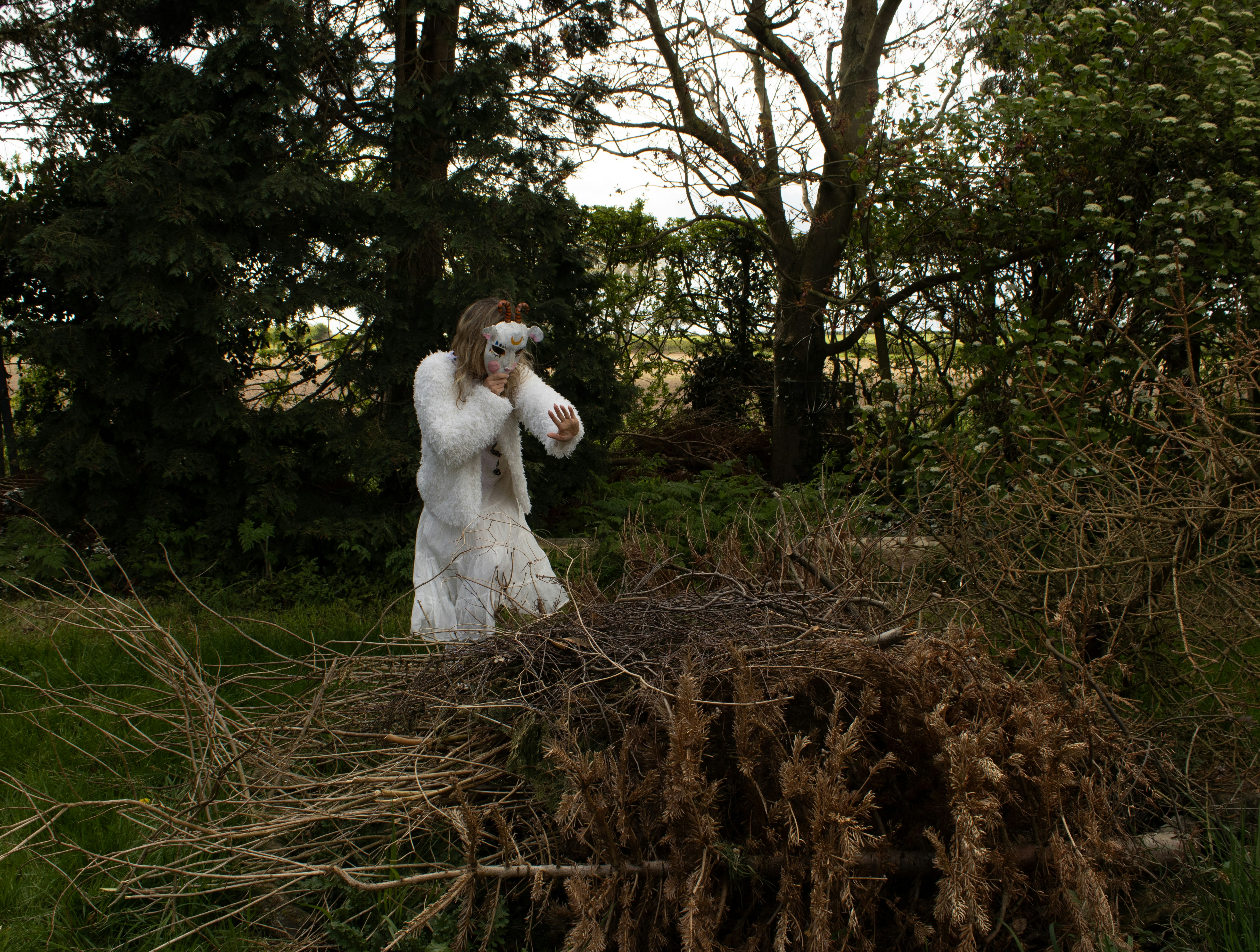 Person in white costume with mask in wooded area