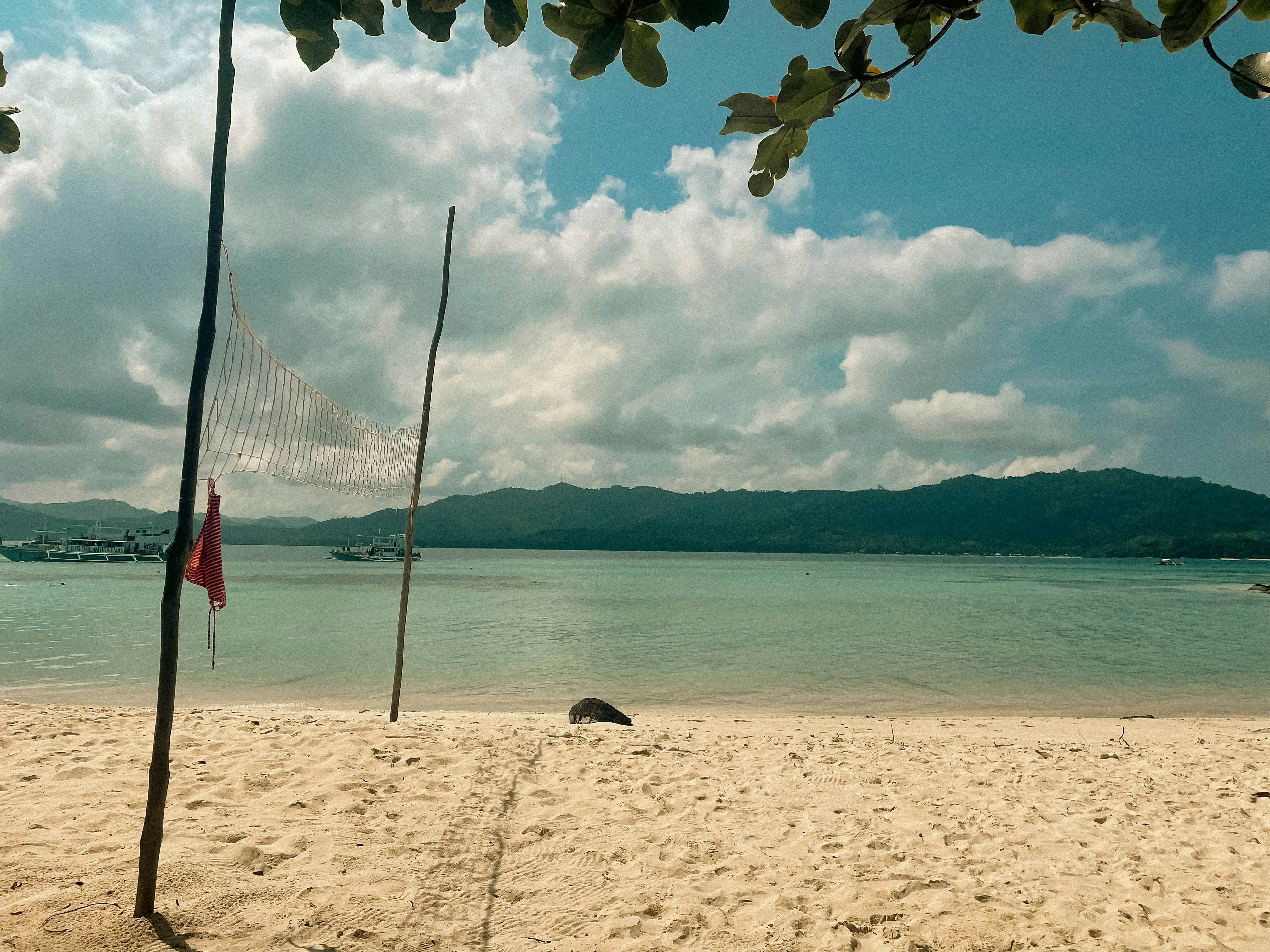 Sandy beach with calm turquoise water and distant hills.