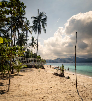 Tropical beach with volleyball net and distant mountains.