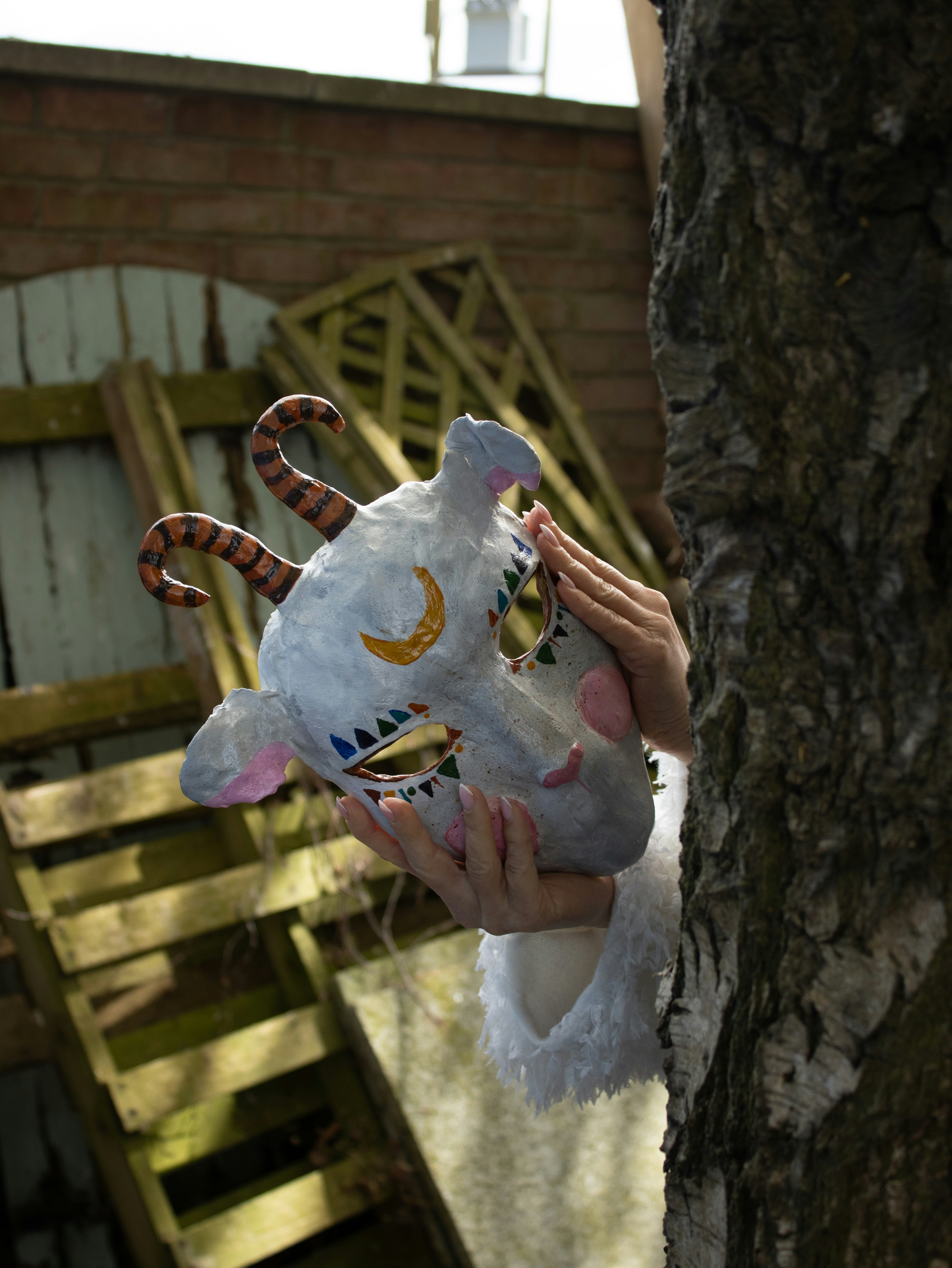 Hands hold a handmade goat mask with horns.