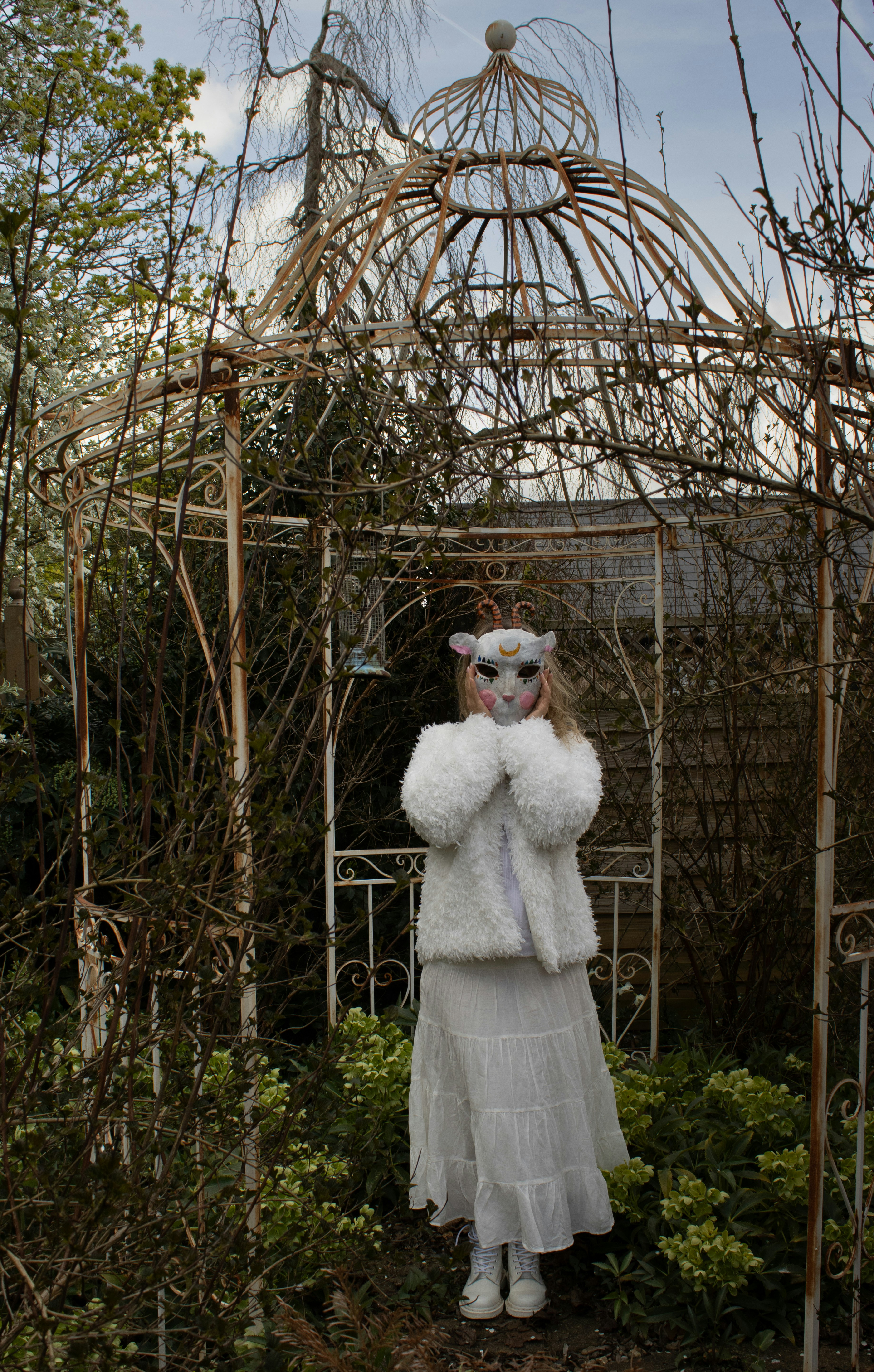 Person in animal mask and white coat in garden.