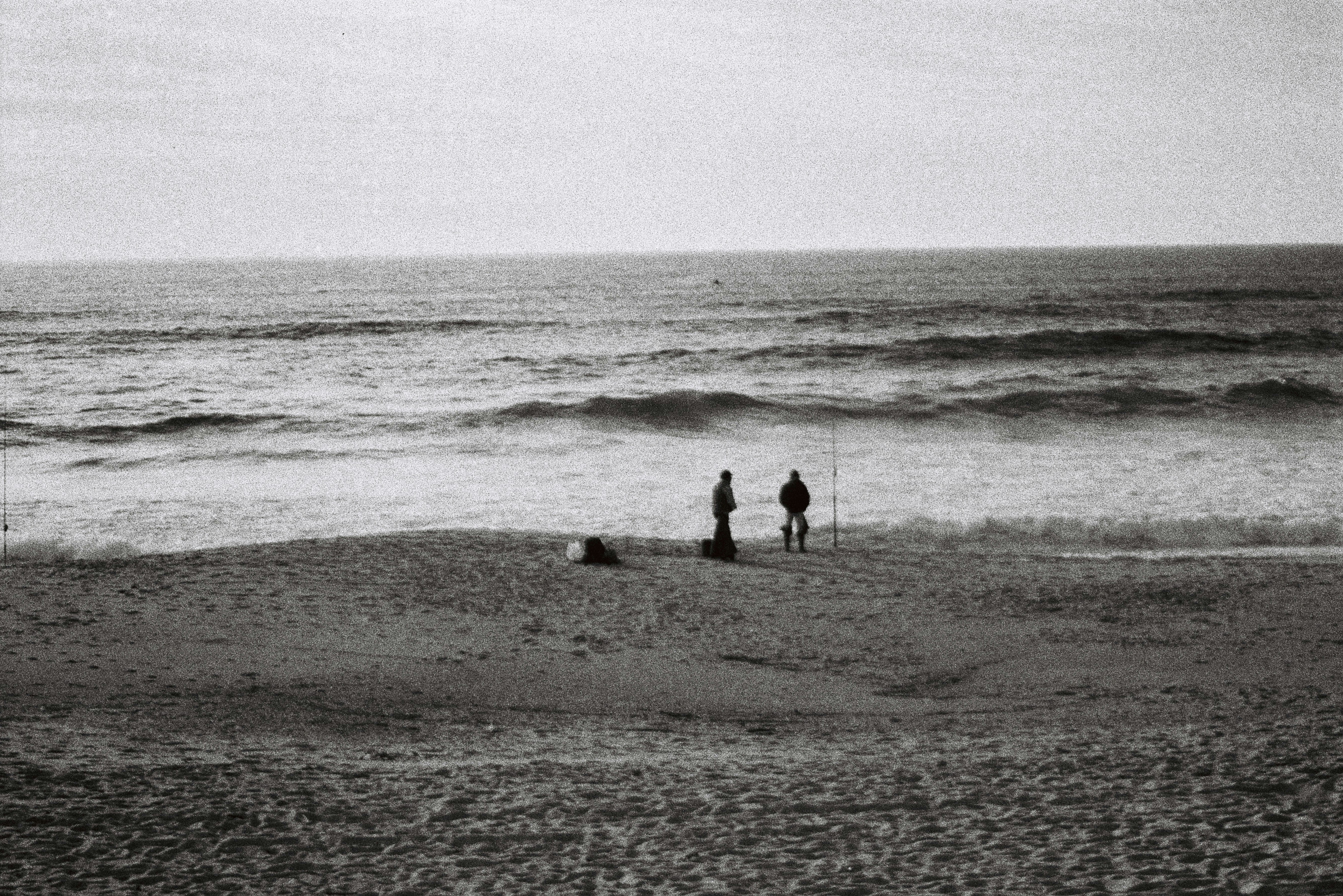 Two people stand on a sandy beach near the ocean.