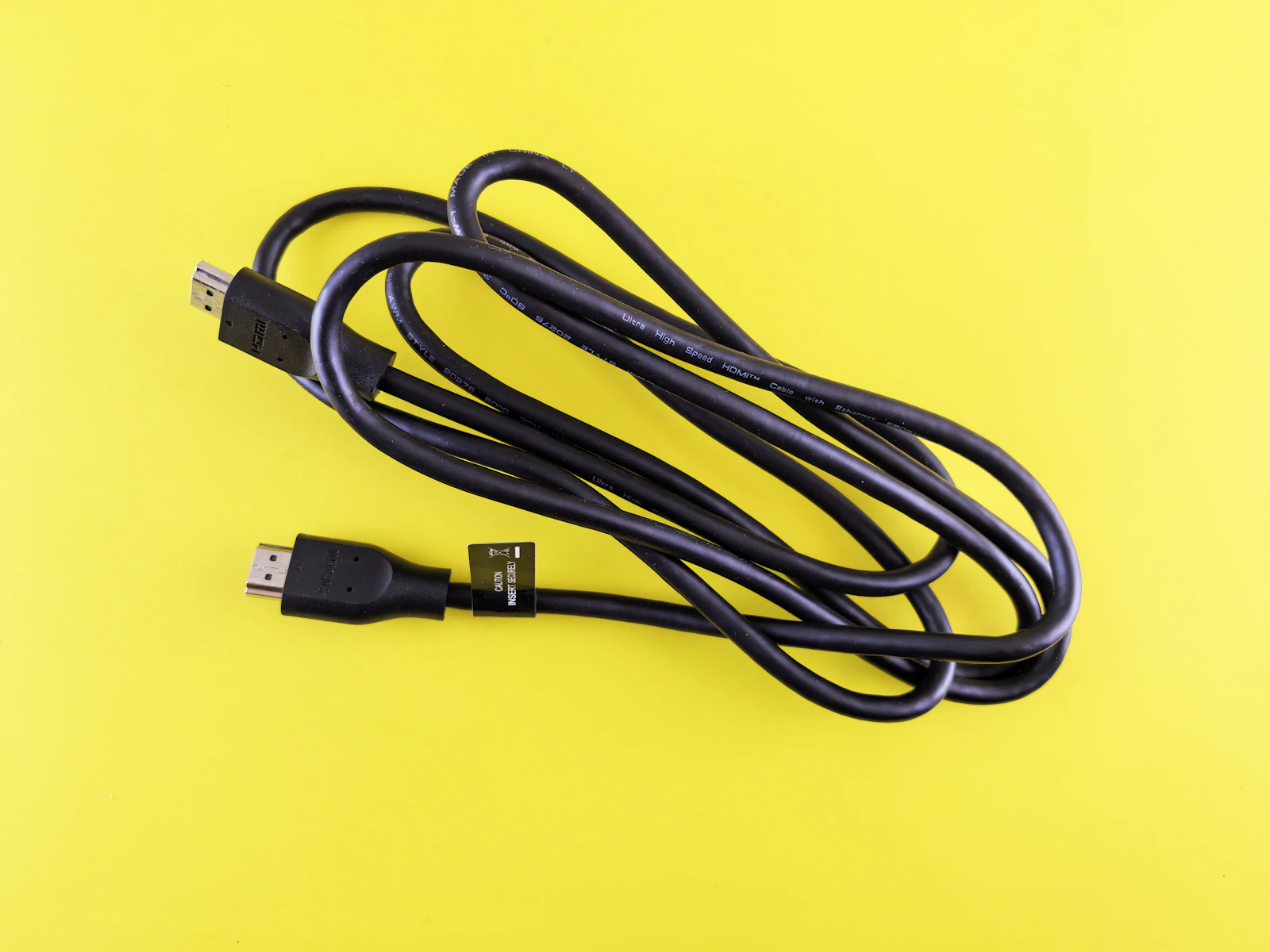 Black Ultra High Speed HDMI cable with Ethernet coiled on a bright yellow background