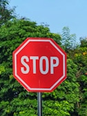 Red stop sign with white lettering against green foliage.