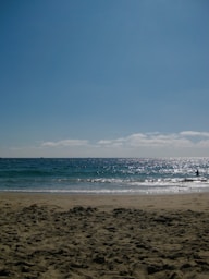 Sandy beach with sparkling ocean waves under blue sky.