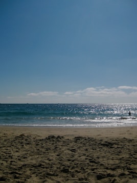 Sandy beach with sparkling ocean waves under blue sky.