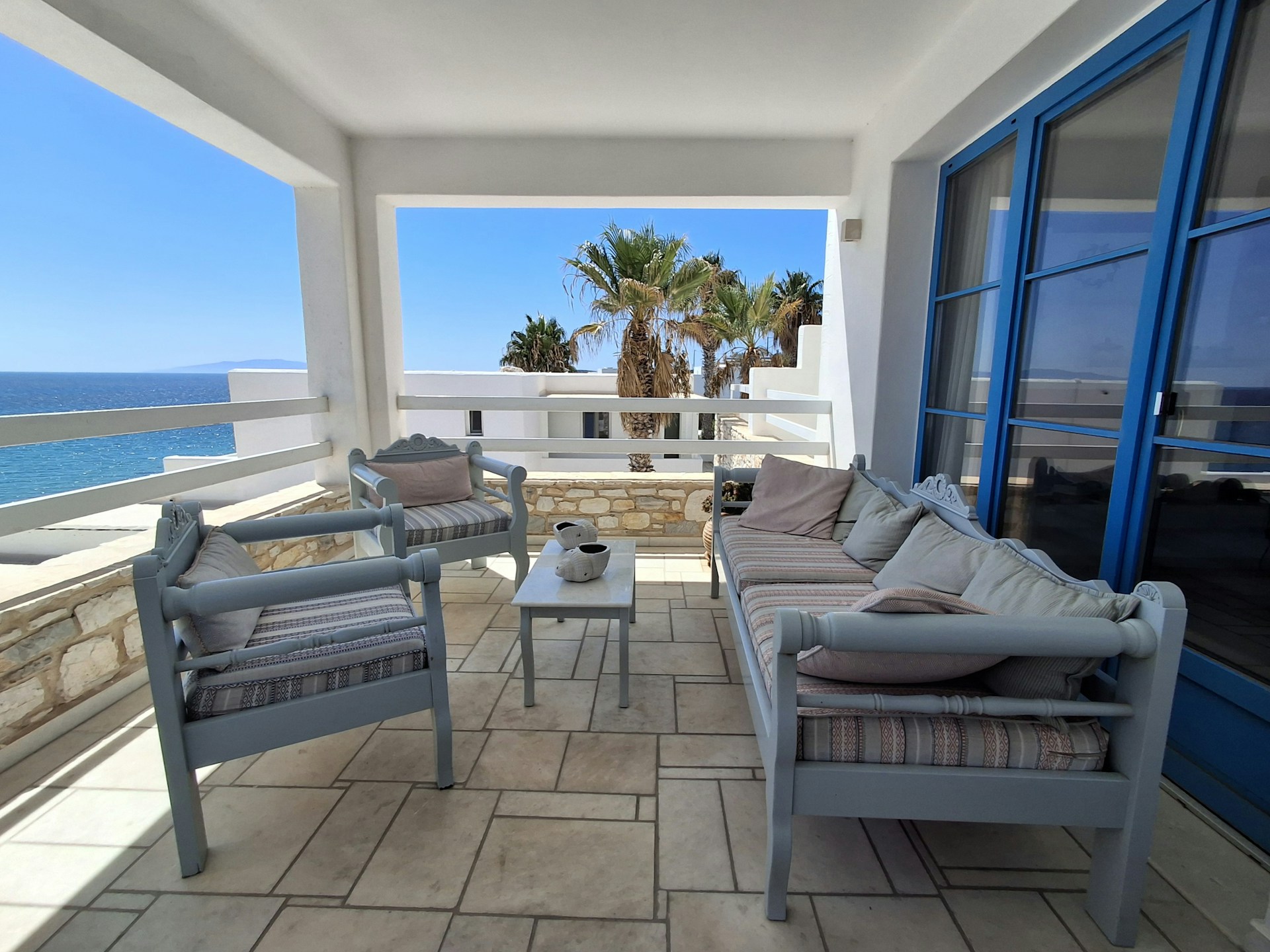 Outdoor seating area with ocean view and palm trees.