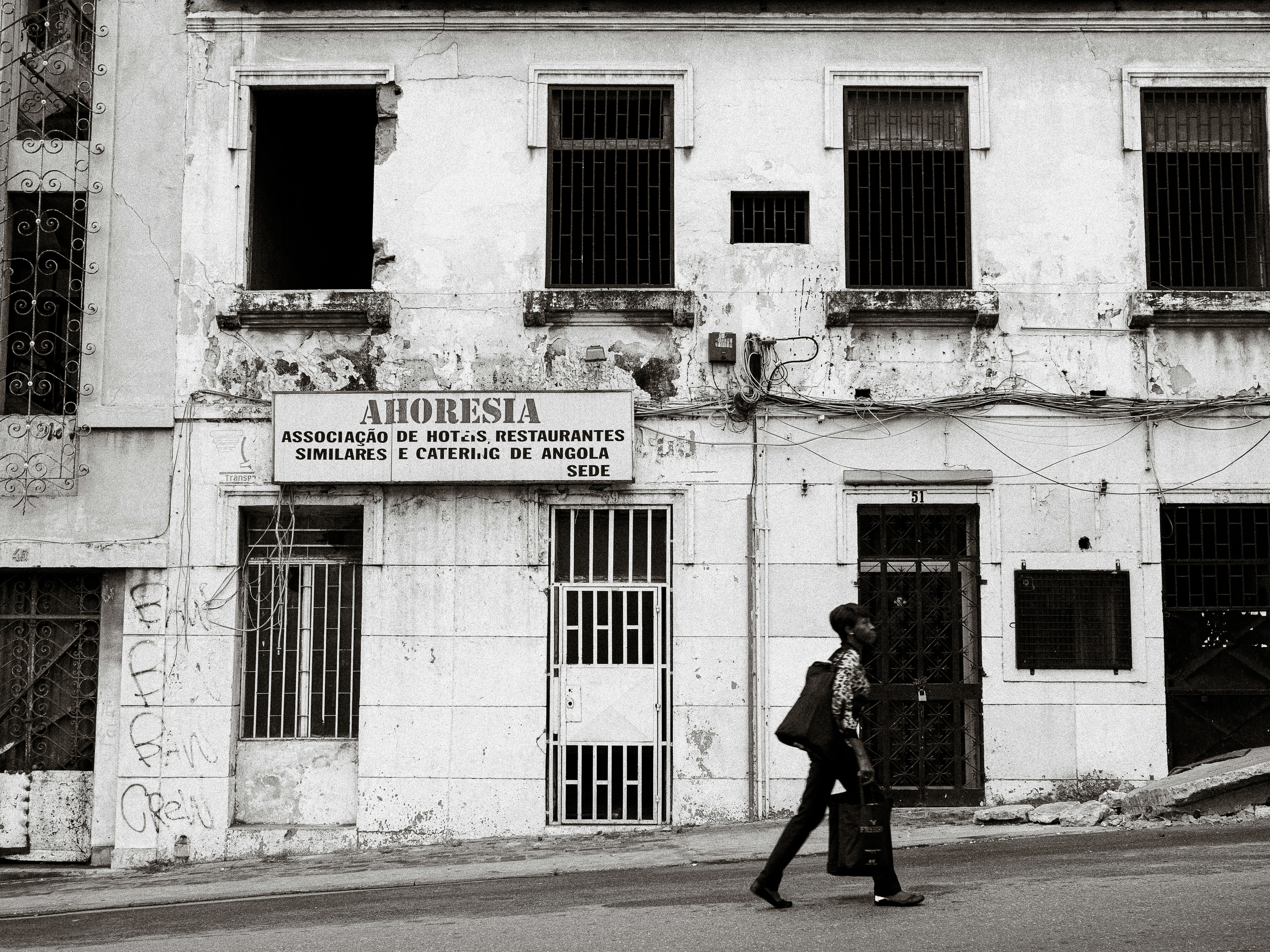 Man walks past a weathered building with barred windows.