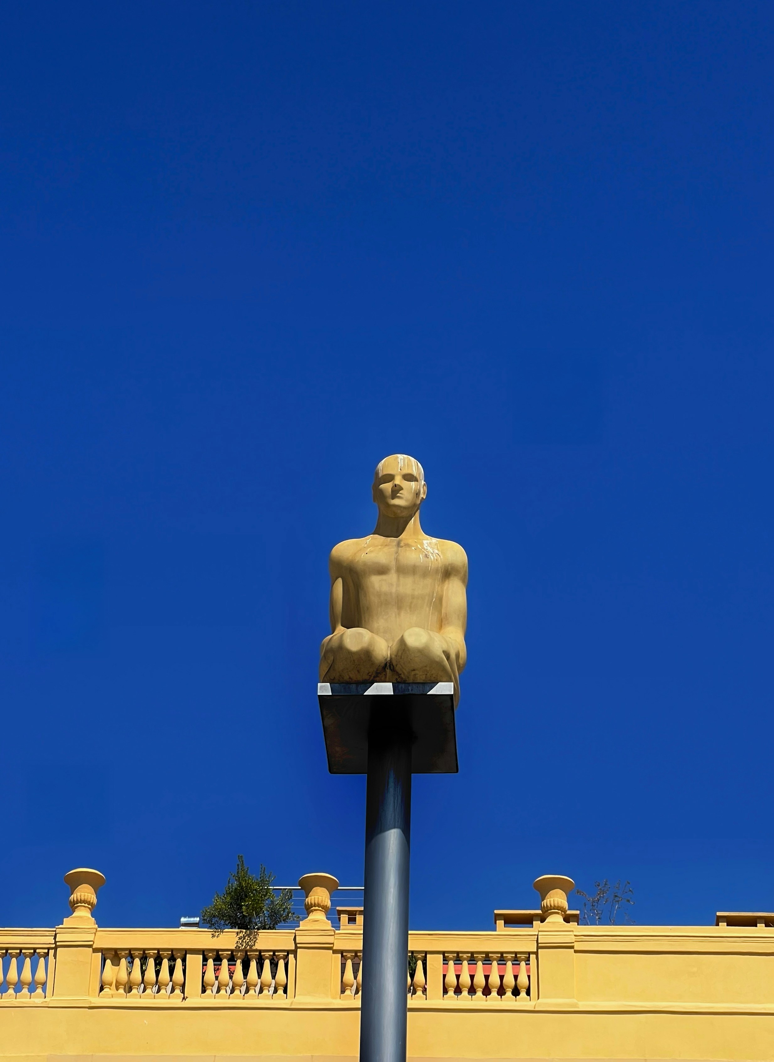 Statue eines sitzenden Mannes vor strahlend blauem Himmel.