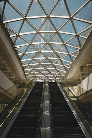Modern escalators leading up to a geometric glass ceiling.