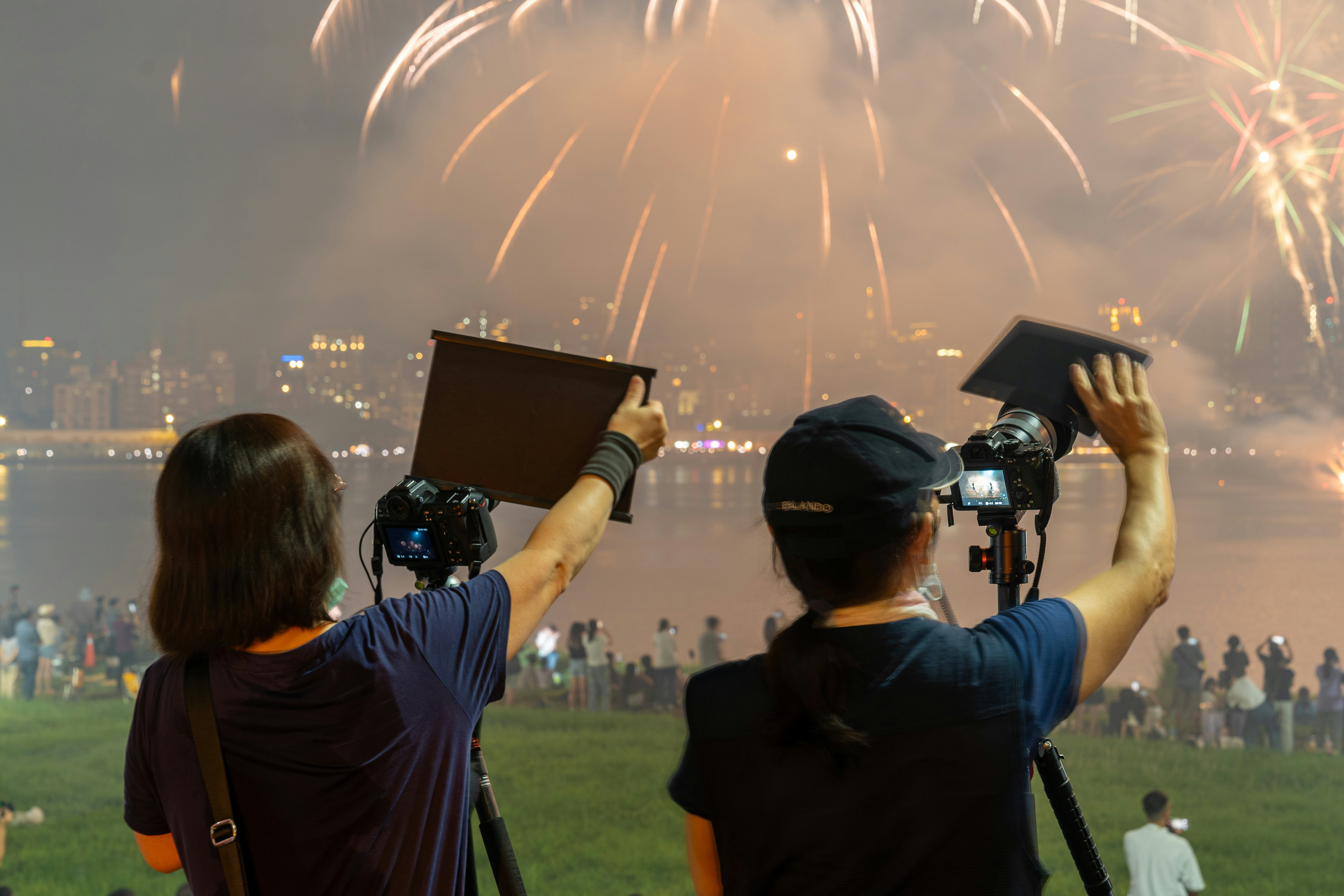 Two people filming fireworks with cameras