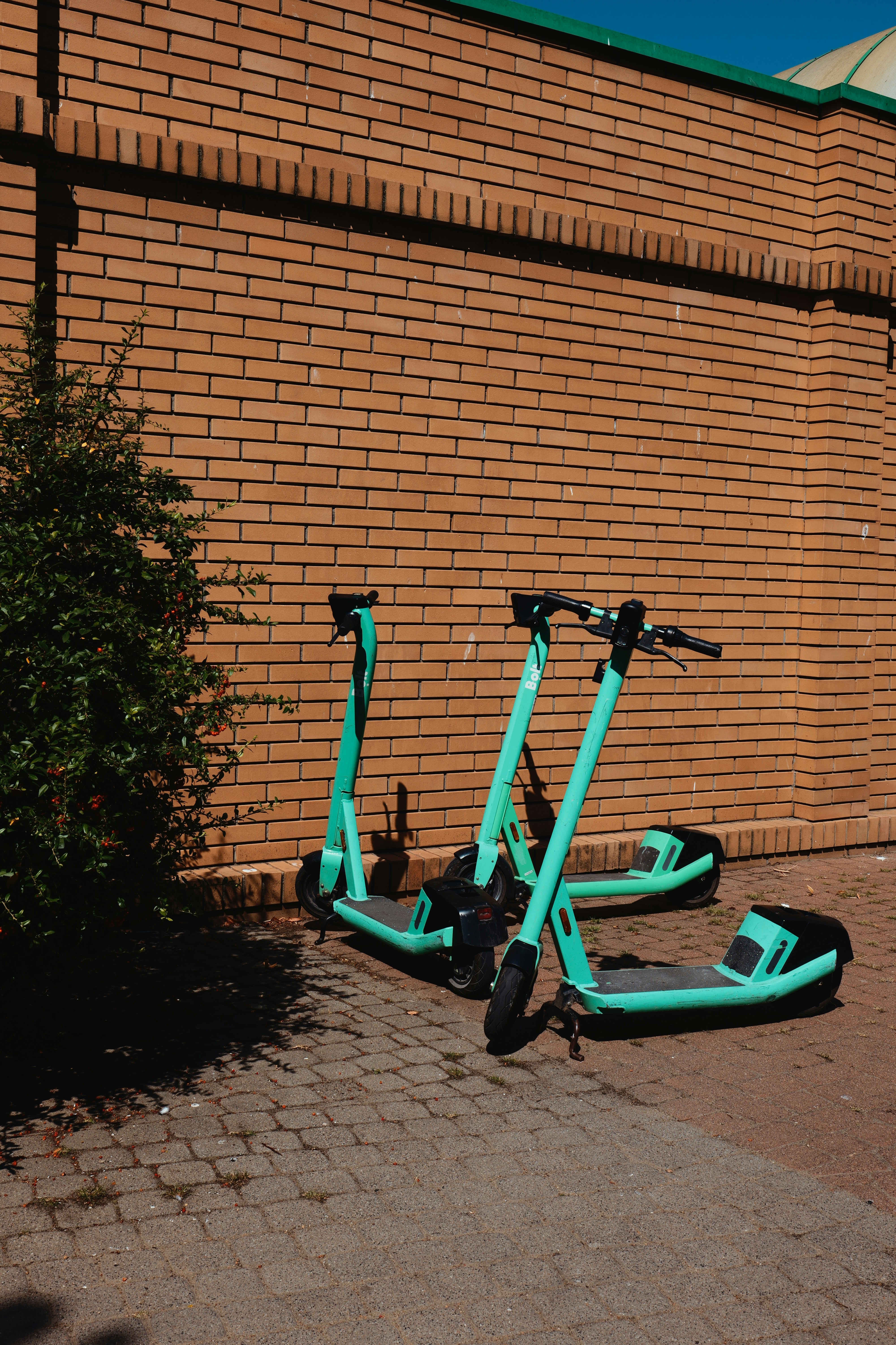 Deux trottinettes électriques turquoise garées près d’un mur de briques