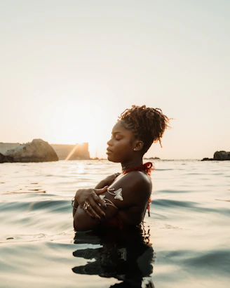Woman in water with arms crossed at sunset