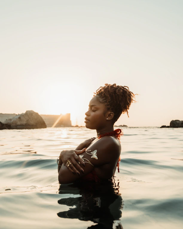 Woman in water with arms crossed at sunset