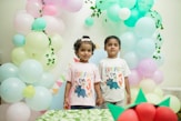 Two children stand by a balloon arch at a party.
