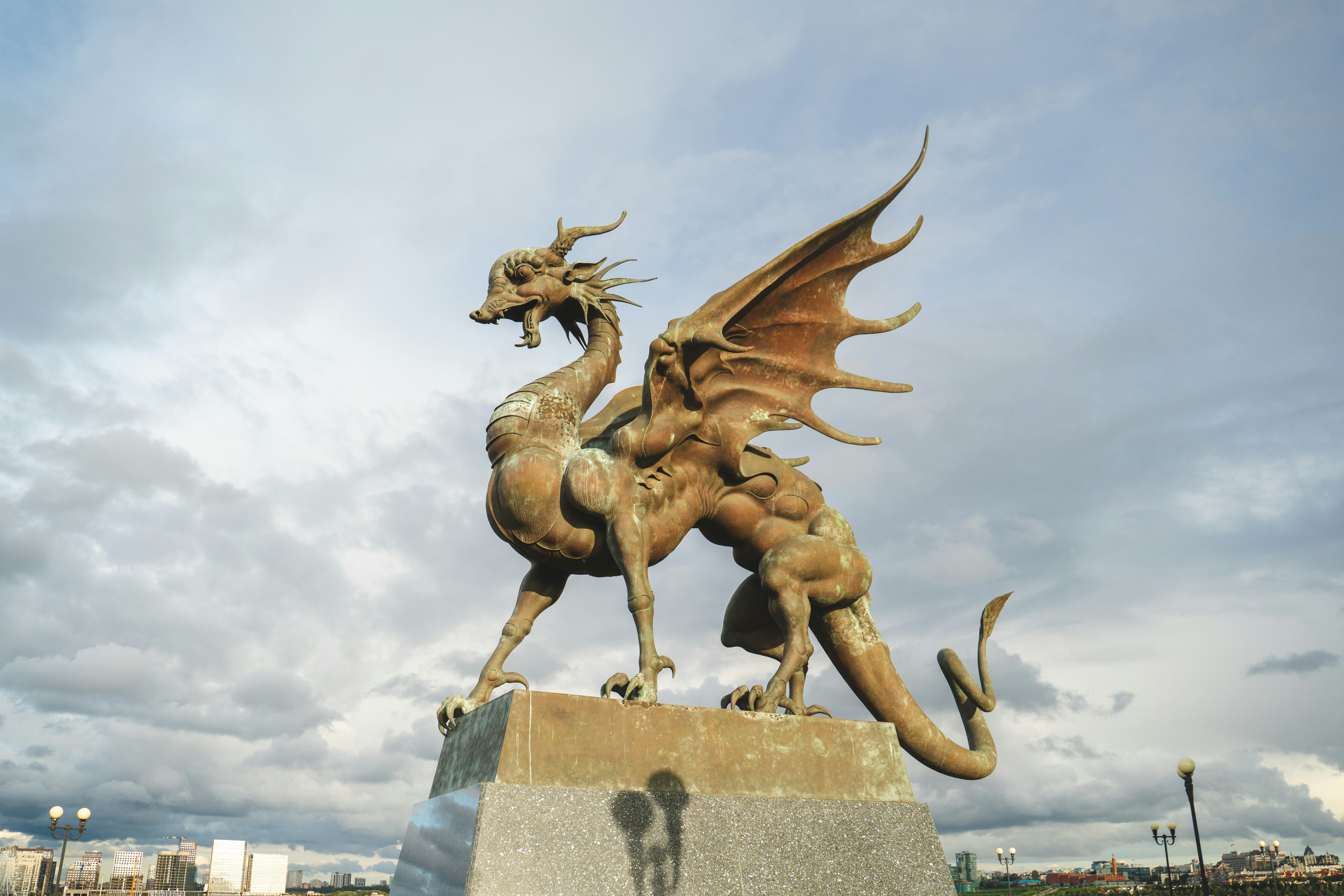 Bronze dragon statue with wings against cloudy sky