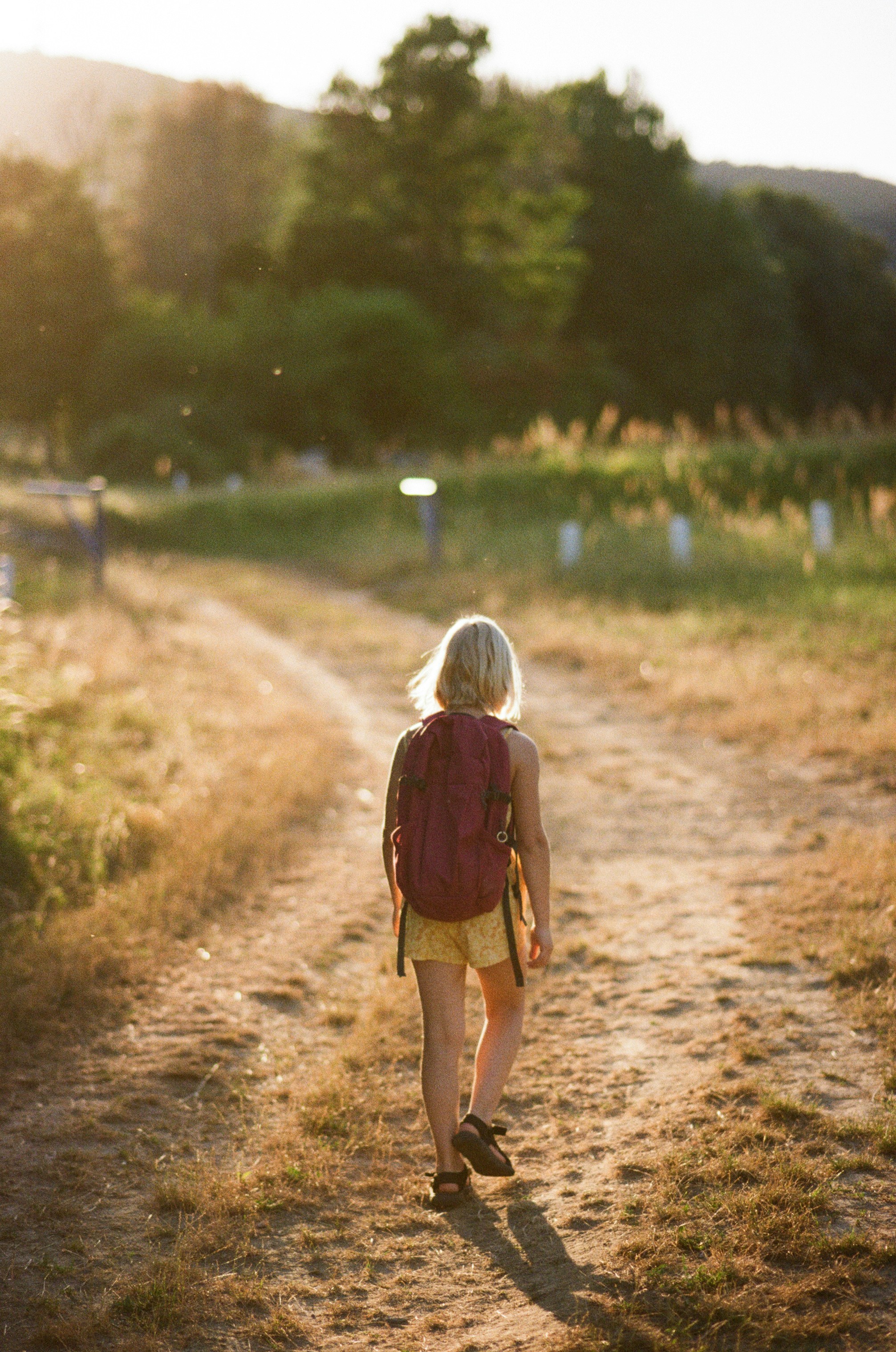 Young girl with backpack walks on dirt path