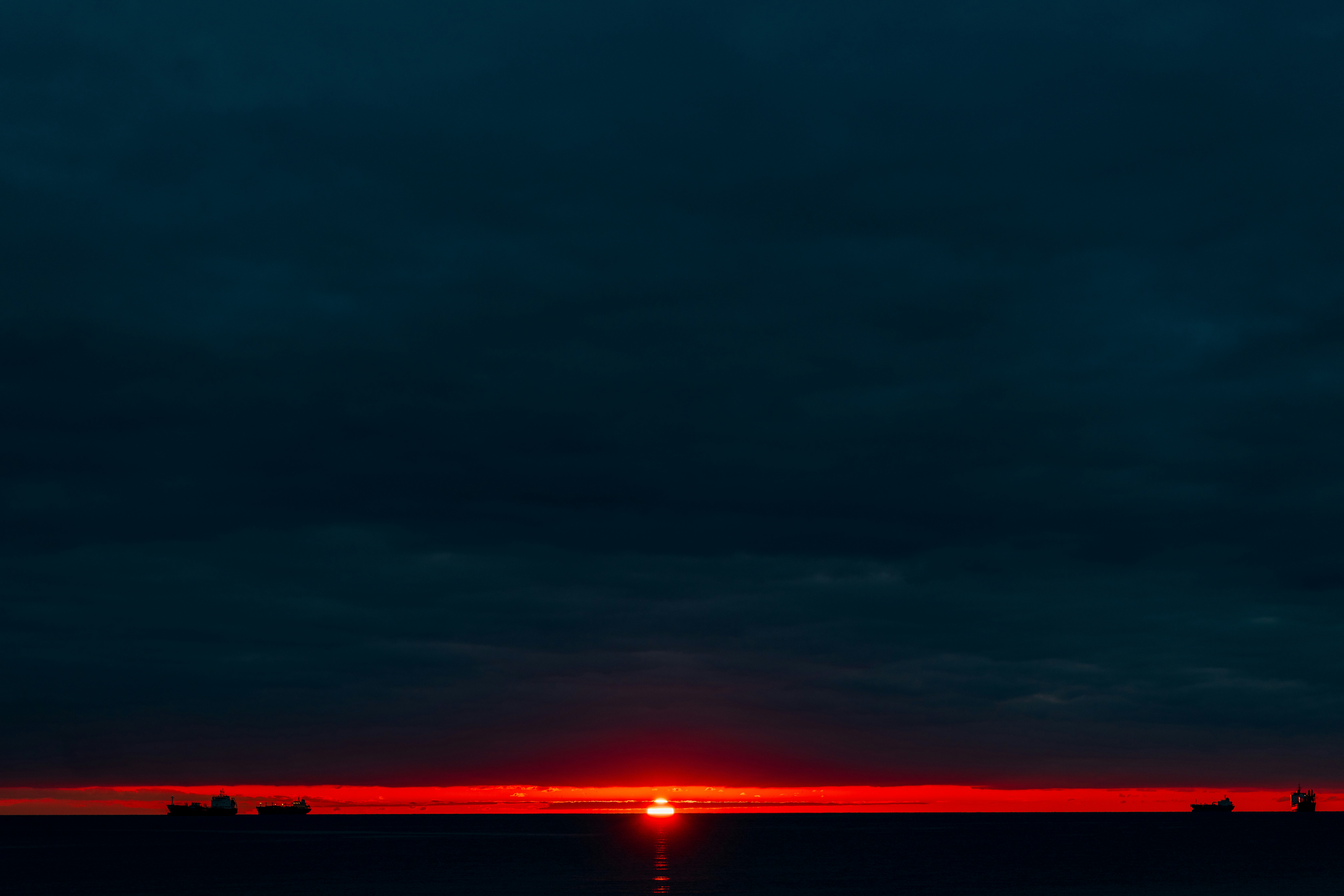 Sunset over a dark ocean with distant ships