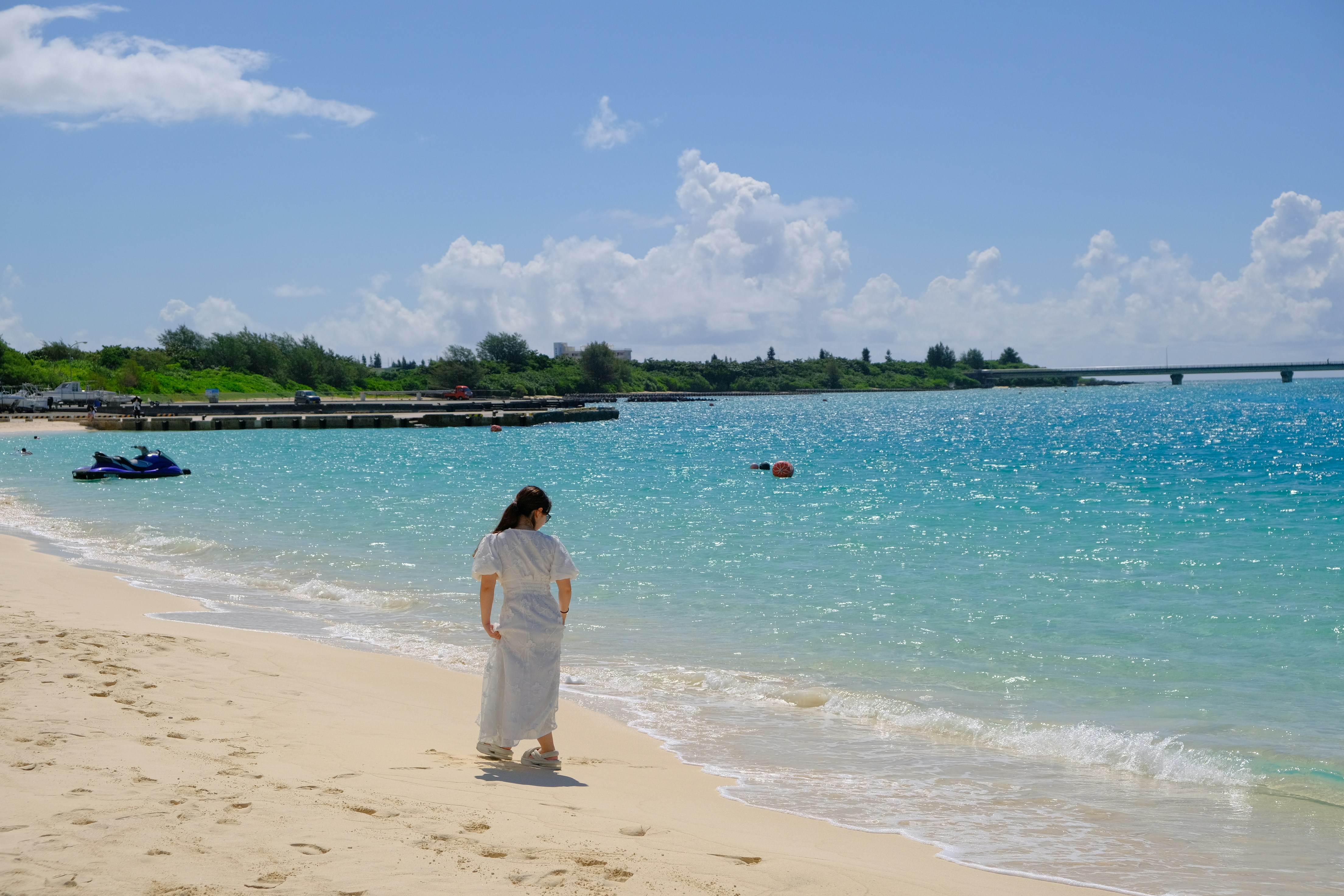 Woman walks along a sandy beach beside turquoise water