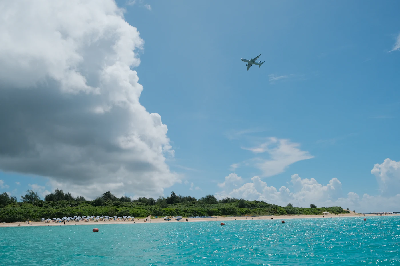 Ein Jet fliegt im Landeanflug tief über die Sonnenschirme am Maho Beach