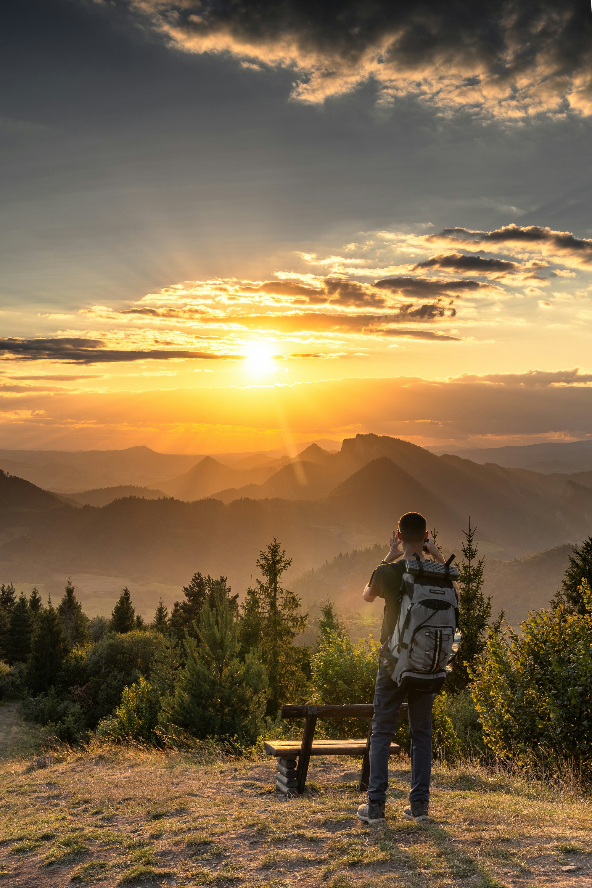 Hiker with backpack watches sunset over misty mountains