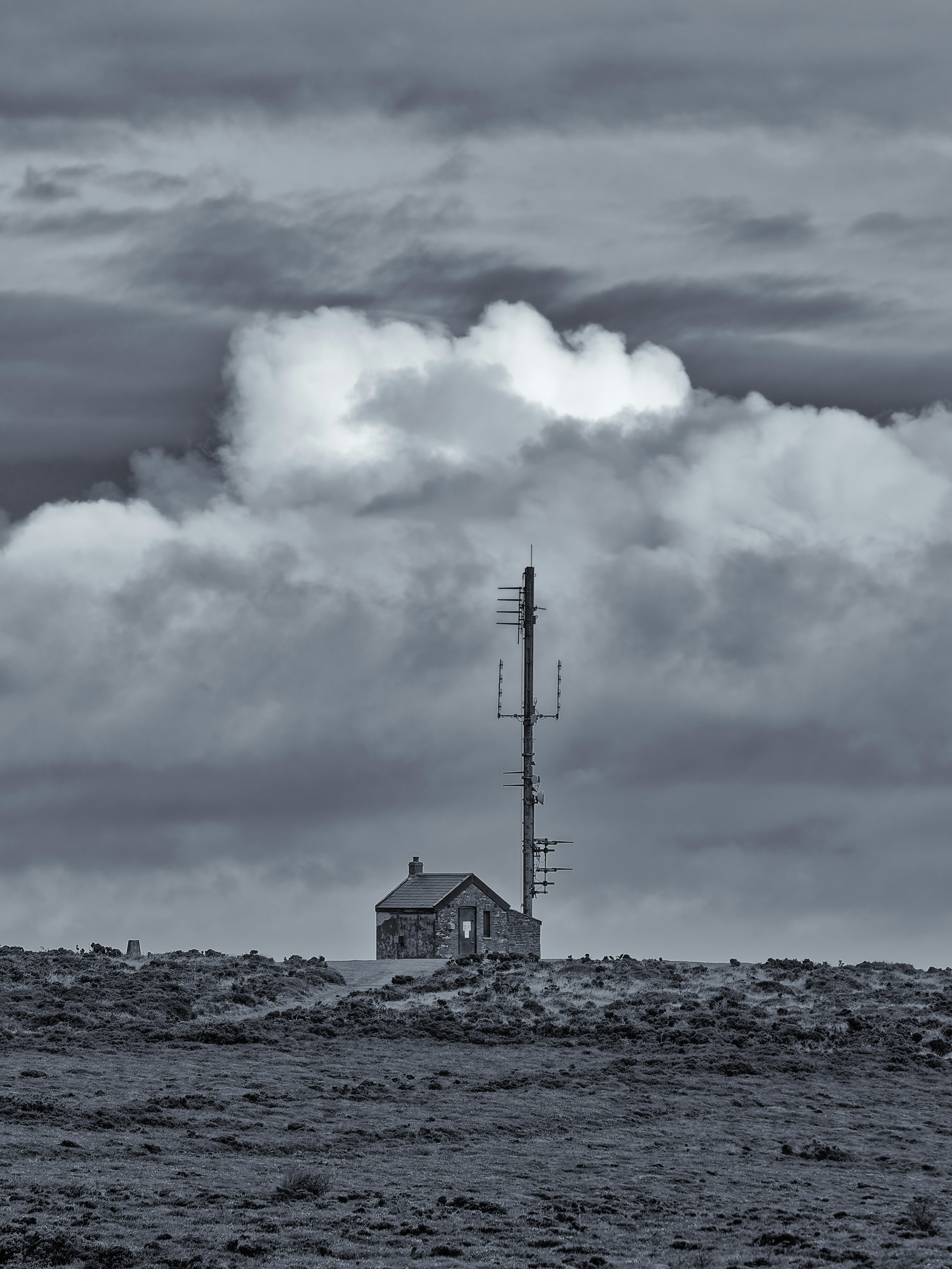 Kleines Steingebäude mit Funkturm unter dramatischen Wolken
