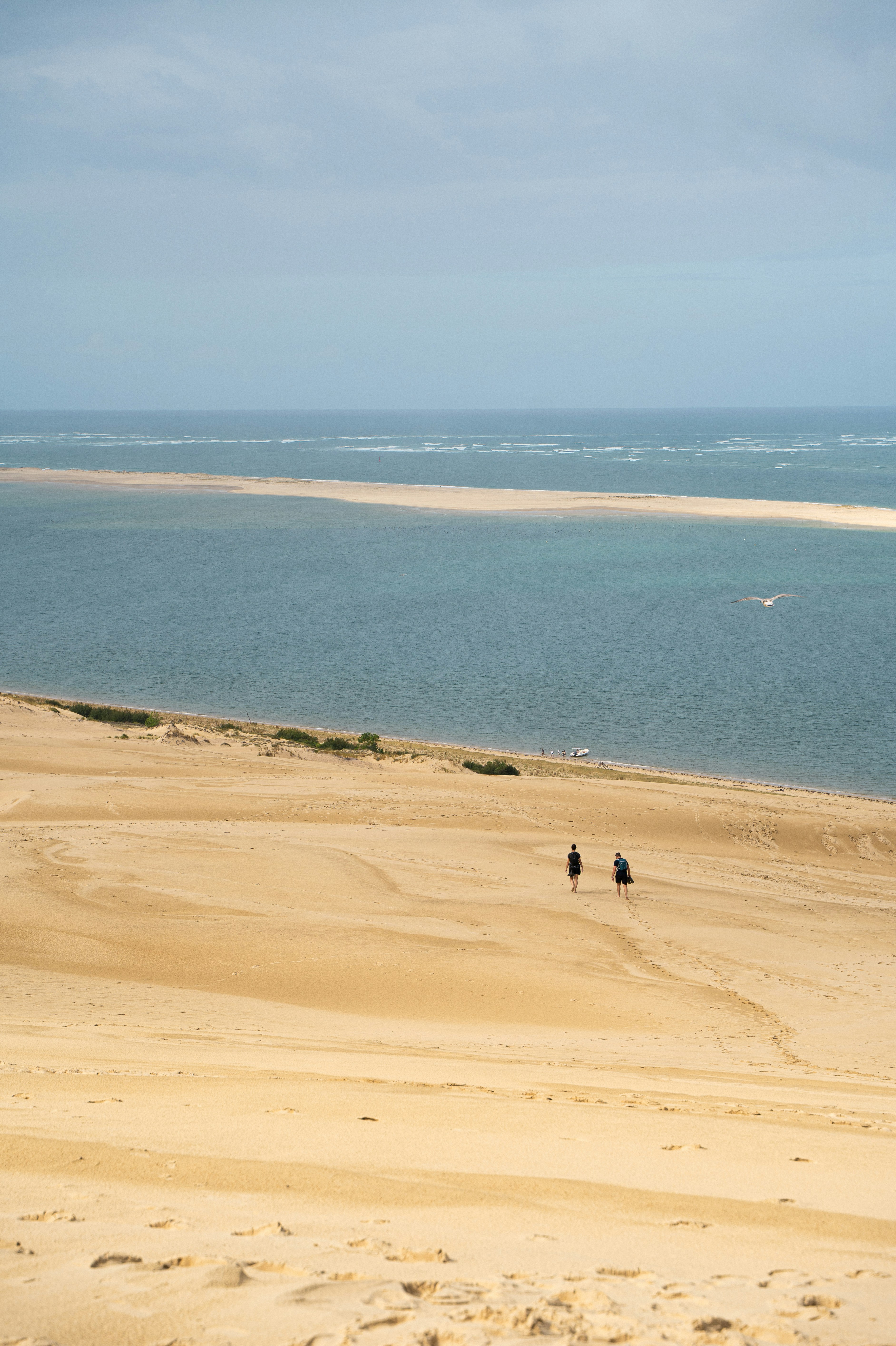 Dos personas caminan por una duna de arena con vistas al océano.