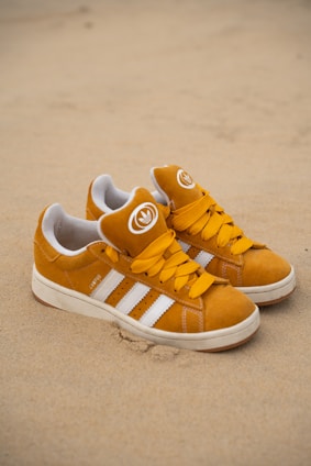 Pair of mustard yellow adidas sneakers on sand.