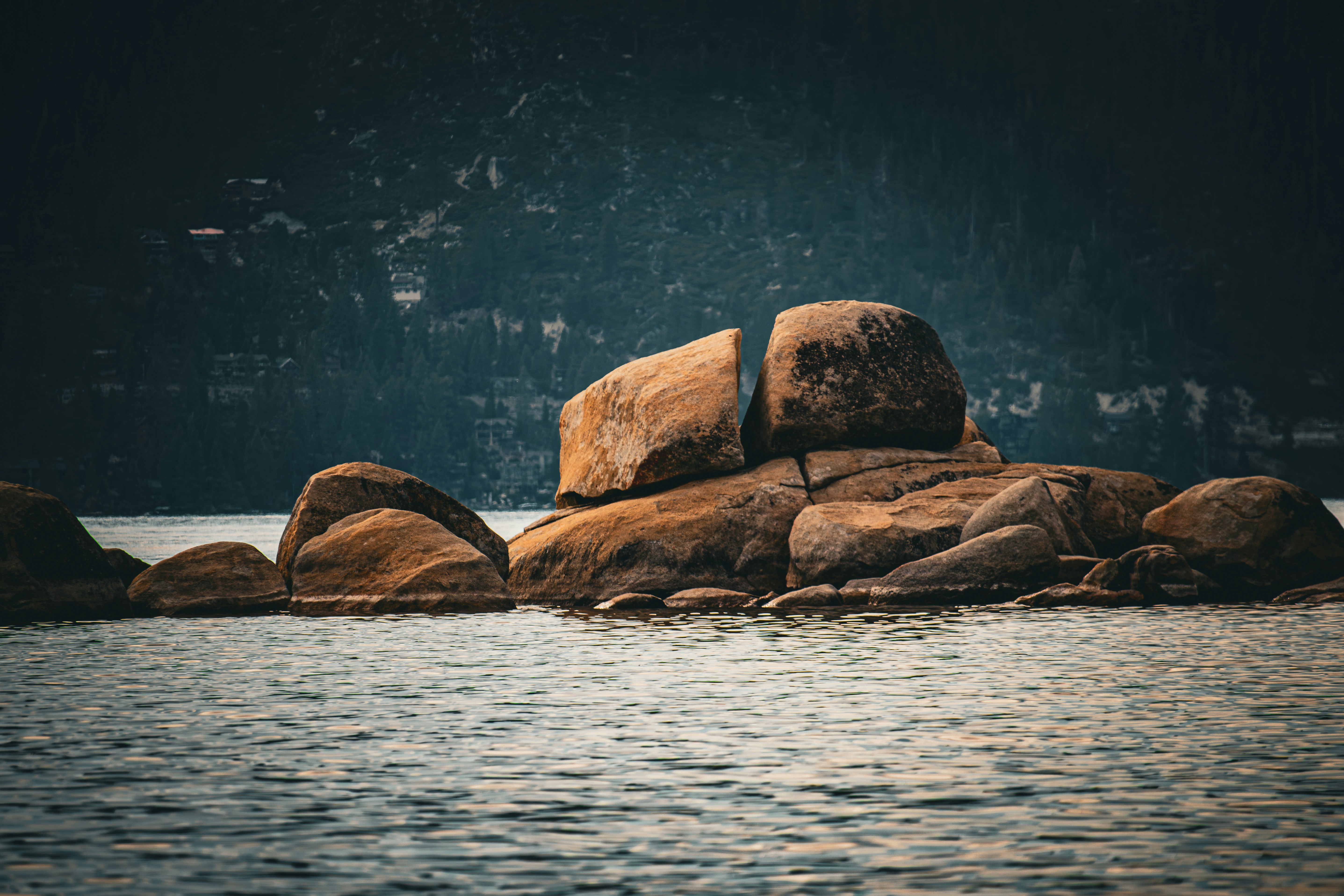어두운 배경의 잔잔한 물에서 큰 바위가 나옵니다.
