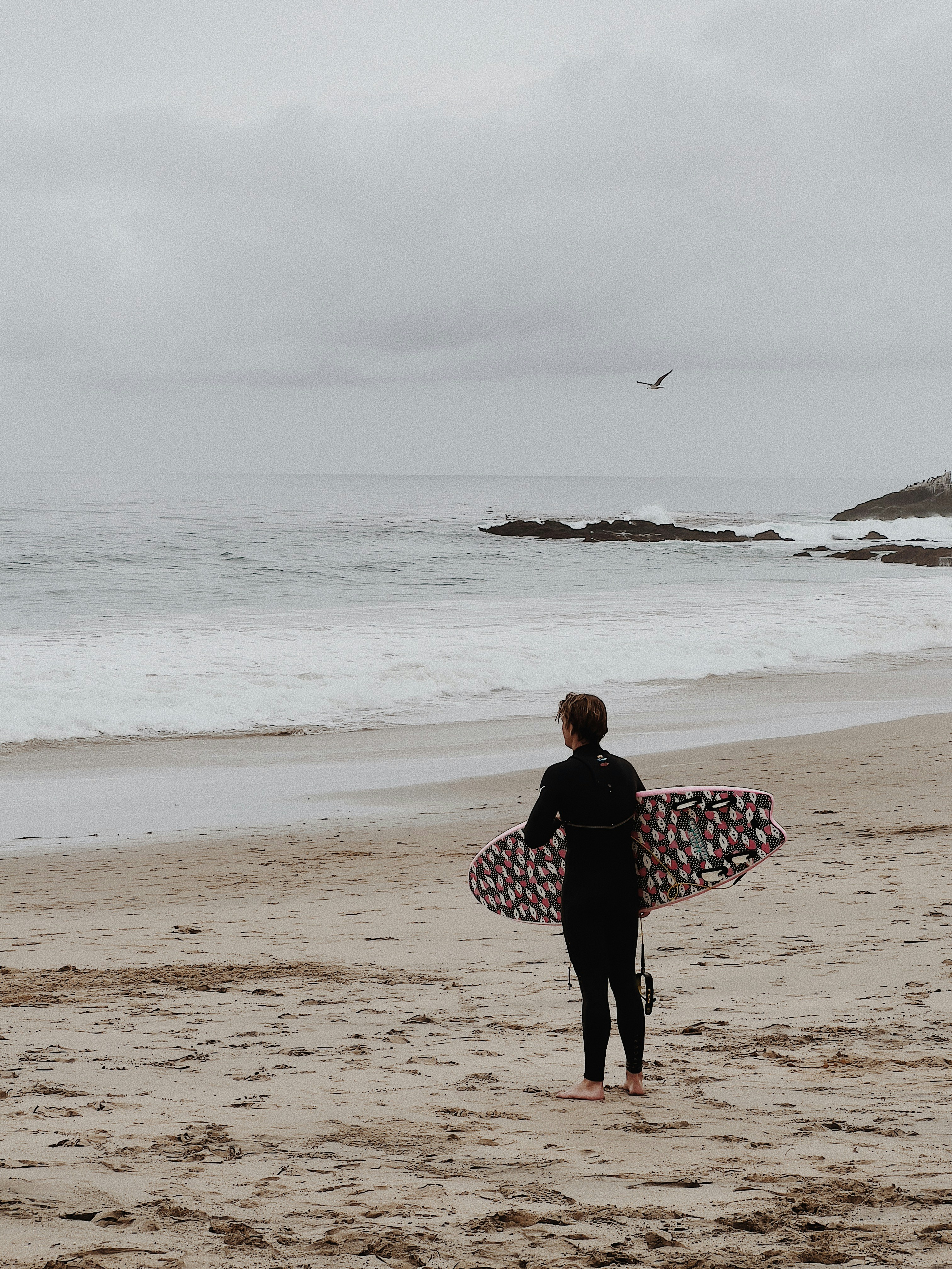 Surfer with surfboard on beach watching waves